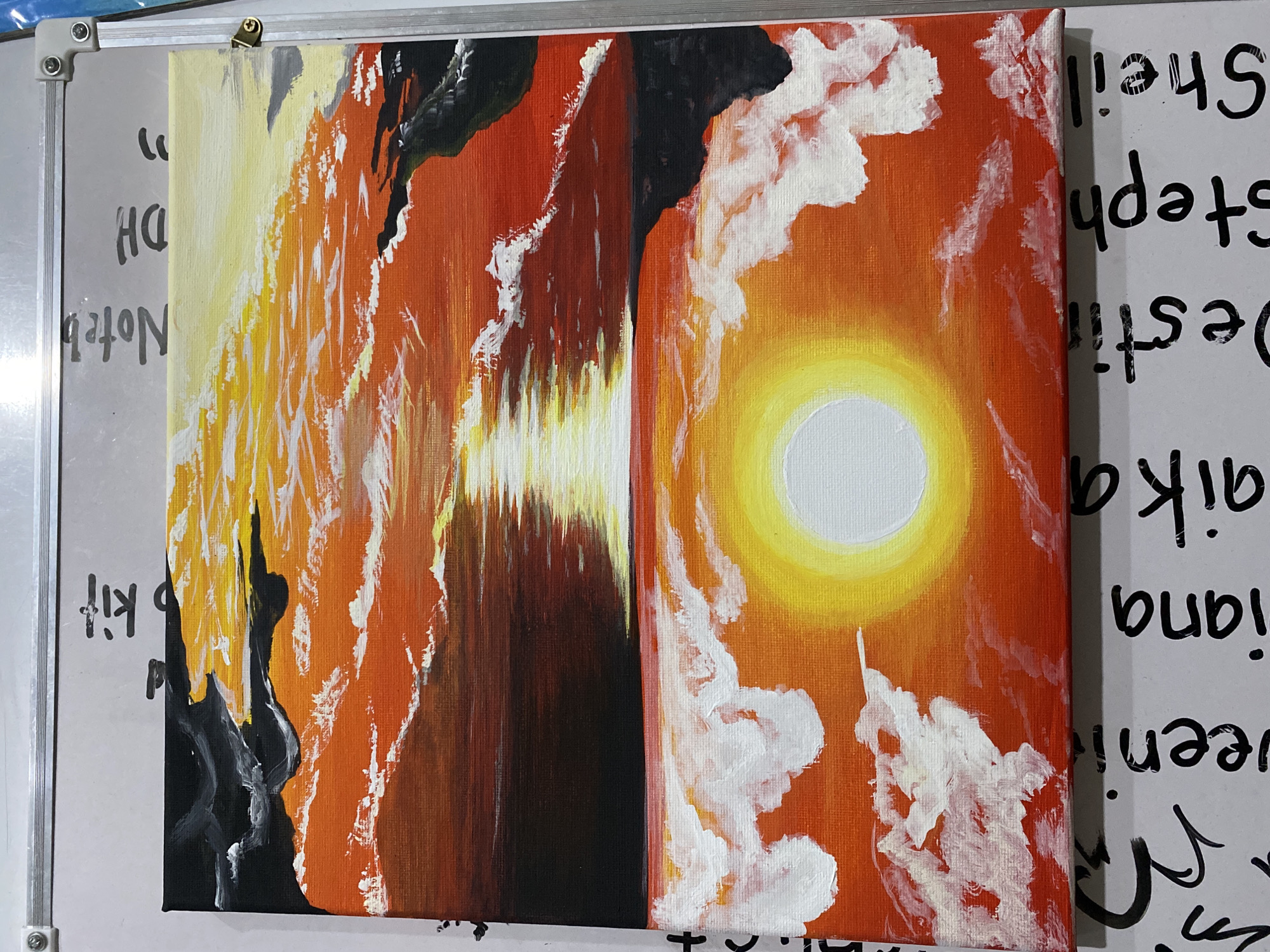 An acrylic painting on canvas, featuring a vibrant abstract or semi-abstract landscape, is propped against a white magnetic whiteboard. The painting is vertically split into two distinct, yet thematically connected, halves.
The left half of the painting is dominated by warm hues of yellow, orange, and red, intermingled with dark black shapes that suggest rugged terrain or abstract forms. Streaks of white paint are prominent, resembling intense light, clouds, or reflections. A central vertical element, composed of bright yellow and white strokes against darker shades, suggests a reflection on water or a striking light source.
The right half of the painting showcases an orange sky with fluffy white clouds of varying sizes. A prominent, bright yellow and white circular orb, representing a sun or moon, is centrally located on this half, radiating light.
The painting's brushwork is visible, giving it a textured appearance. The overall color scheme is warm and dynamic, contrasting intensely bright areas with darker tones.
In the background, the white whiteboard is partially visible on both sides of the painting. It has a metallic frame along its edges. Black handwritten text in marker is visible on the whiteboard. On the left, partially obscured and possibly rotated, are words like "DH," "Noted," and "kit." On the right, written vertically and mostly upside down, are names such as "Shelia," "Stephi," "Destin," "liana," and "ka." No human figures or direct activity are depicted in the image, which captures the painting in an indoor setting.