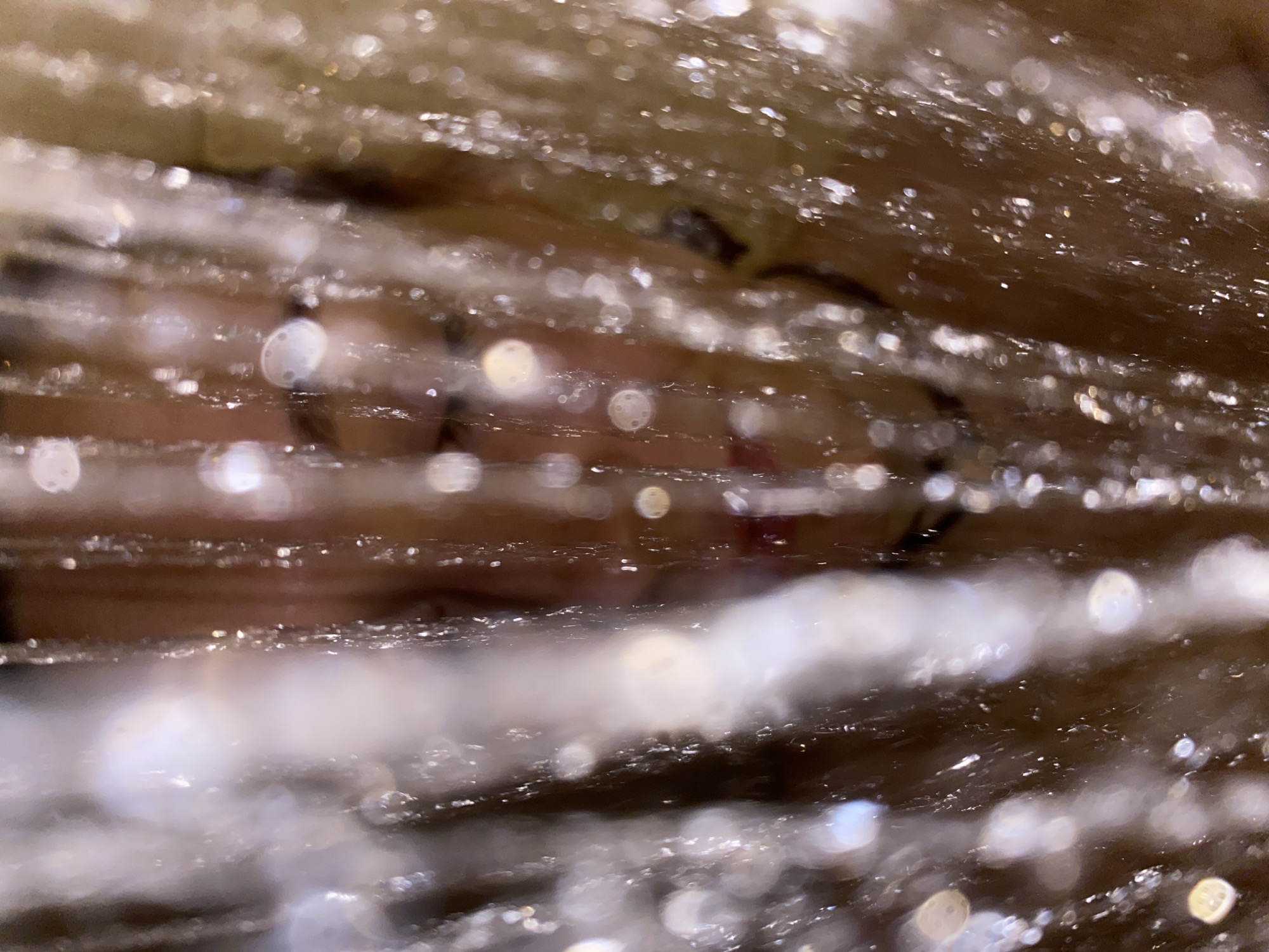 The image shows a blurred view of a person's face through what appears to be a wet or covered surface. The person has glasses and their lips are visible. The background and foreground are heavily out of focus, creating a bokeh effect with numerous light spots. The location in the city of Chaikovsky, Russia is not discernible from the image.