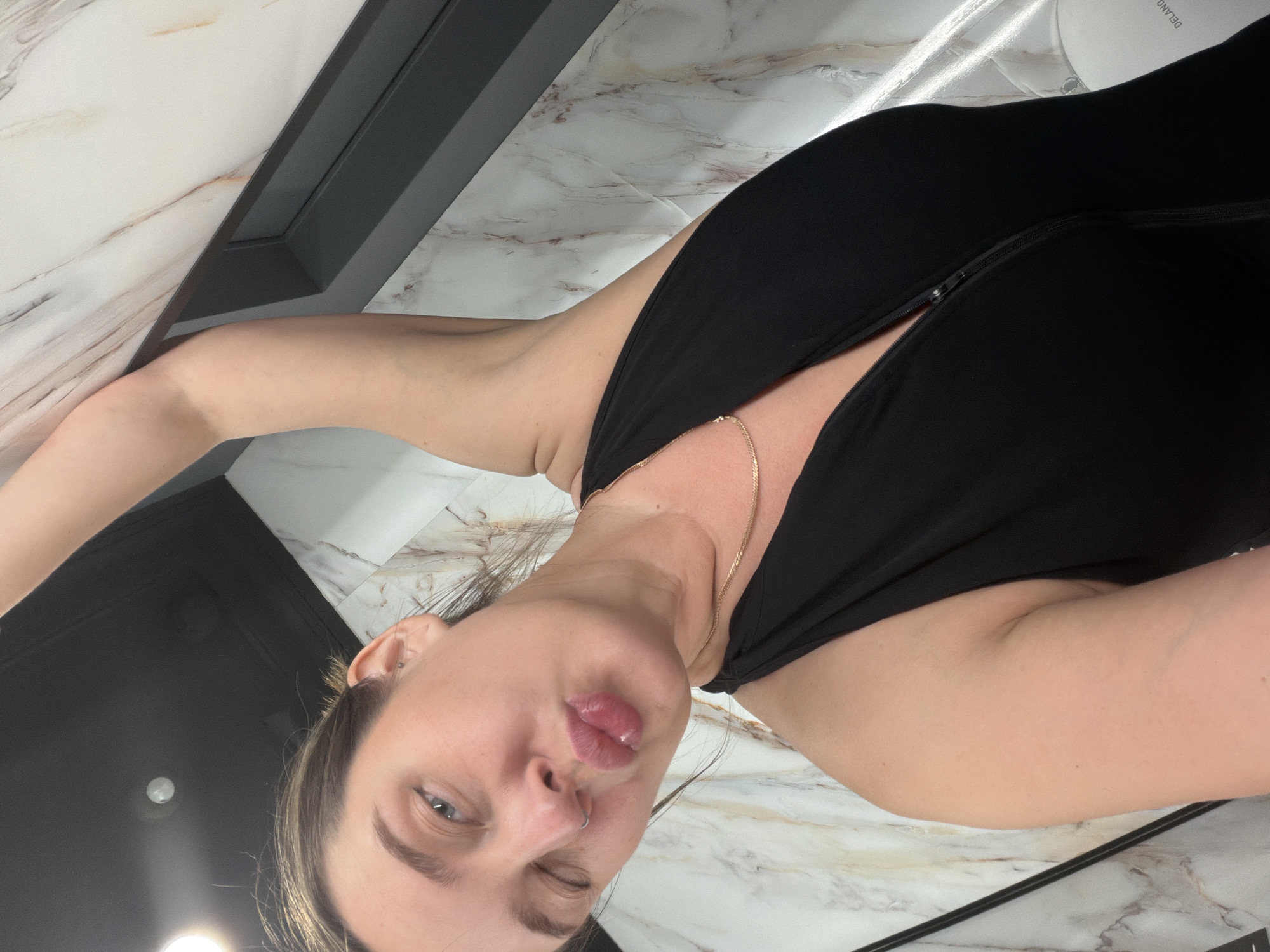 A woman winks at the camera with puckered lips. She wears a black top and a gold chain necklace. The background includes a marbled surface and a black frame. The word "DELAND" is partially visible in the upper right corner. There is no indication of the location being Moscow, Russia.