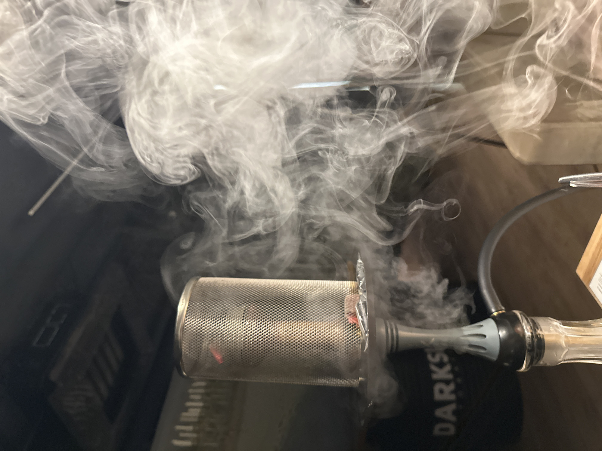 A close-up shot of a hookah, with thick white smoke billowing around it. The hookah's metal bowl, filled with burning material, is visible, along with the hose and mouthpiece. The environment around the hookah is blurry and unclear. There is no evidence that suggests this image was taken in the city of Chaikovsky, Russia.