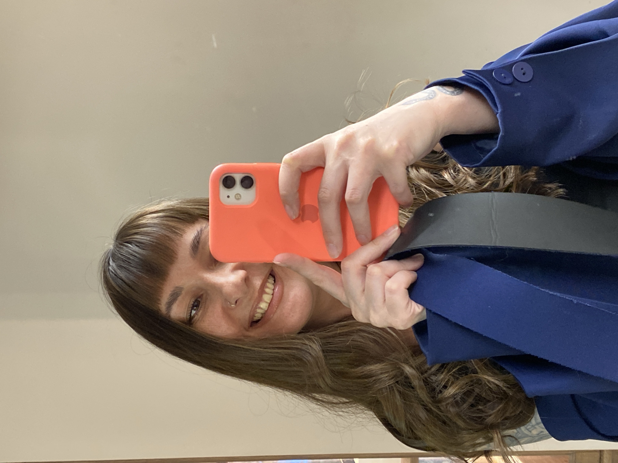 A person is taking a selfie in what appears to be an indoor setting. The person has brown hair, a fringe, and is wearing a blue jacket. They are holding an orange mobile phone, partially obscuring their face. The location in Votkinsk, Russia, cannot be determined from the visual information provided.