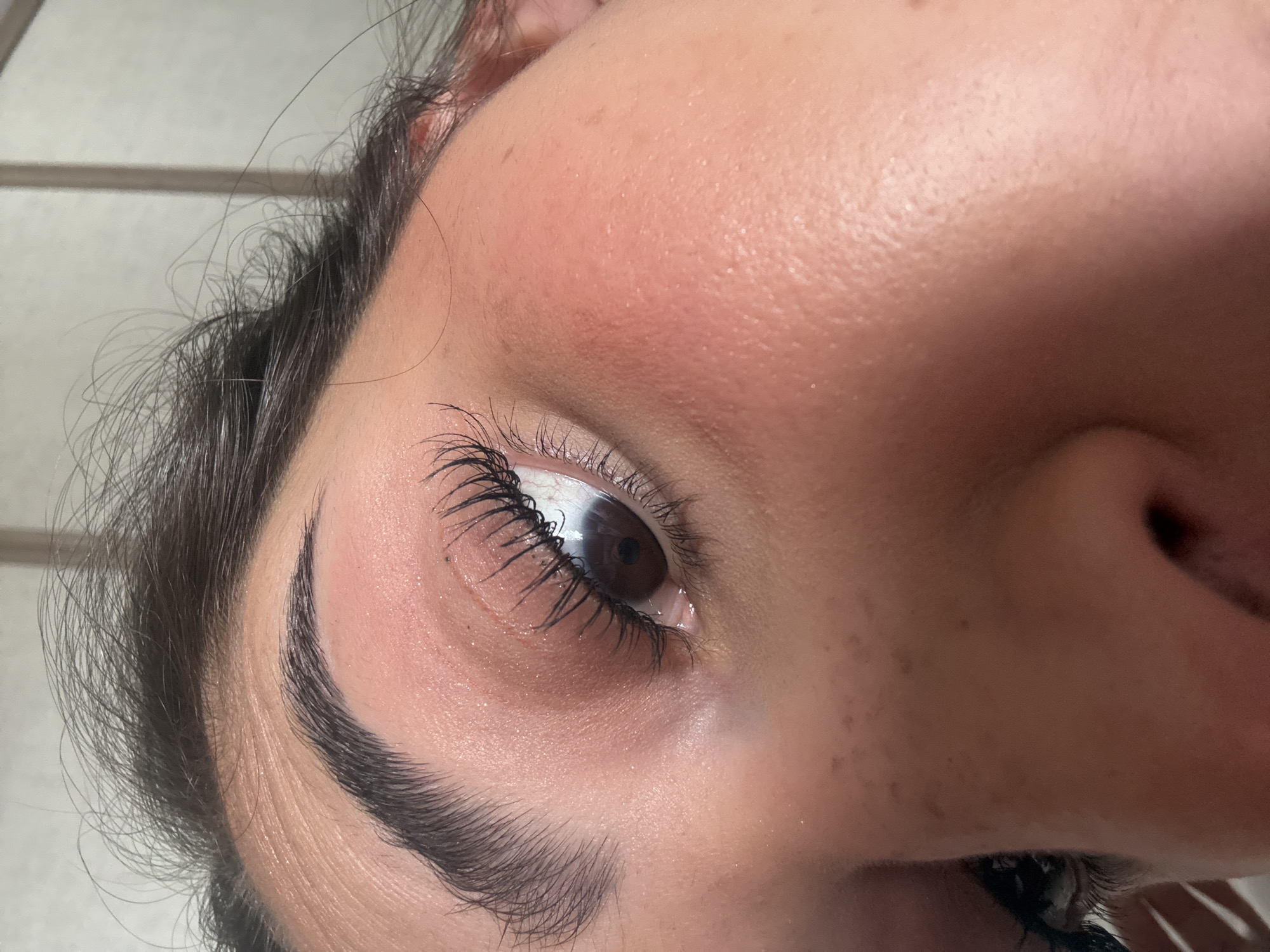 A close-up, angled shot of a person's face focusing on their eye, eyebrow, and part of their nose. The eye is brown with dark lashes. The eyebrow is dark and shaped. The skin tone is light with some freckles visible. The environment is not discernable enough to determine a specific location in San Bernardino Tlaxcalancingo, Mexico. The scene primarily features a portrait of facial features.