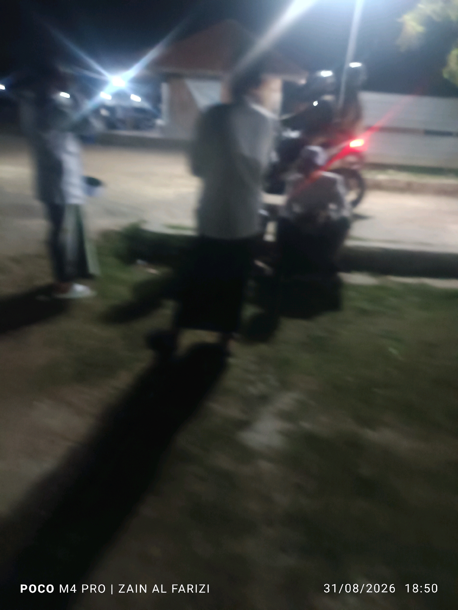 The image captures a night scene in Bancaran, Indonesia. The focal point is a person standing near a motorcycle. Another person is partially visible in the background. The environment appears to be an outdoor area with some lighting, suggesting it might be a street or a public space. The overall image quality is low due to blurriness and low light conditions, making it difficult to discern finer details. The timestamp "31/08/2026 18:50" is visible in the lower right corner, and the text "POCO M4 PRO | ZAIN AL FARIZI" is present in the lower left corner.