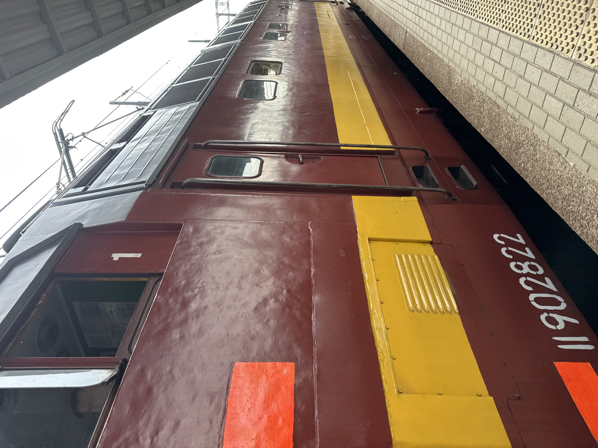 A side view of an electric locomotive in Nizhny Novgorod, Russia. The locomotive is painted in dark red with a broad yellow stripe. The number "II 902822" is painted on the side. The locomotive is parked next to a platform wall. The locomotive has a rectangular window. A sign of "1" is beside the window. Overhead catenary wires can be seen.