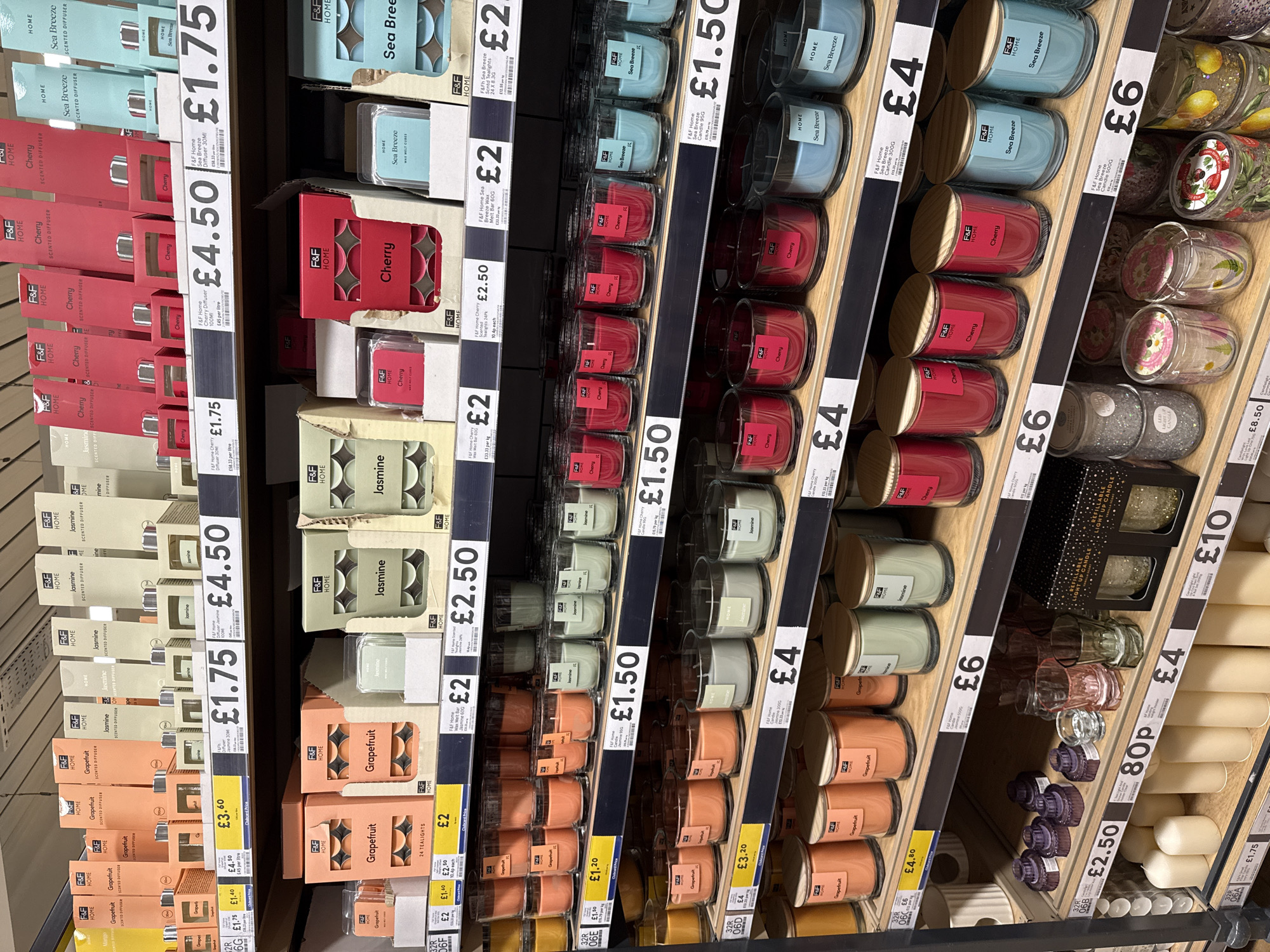 The image shows shelves stocked with scented candles and diffusers in what appears to be a retail environment, likely a supermarket or department store. The items are organized by scent and price, with "F&F Home" branding visible. The products are arranged by price point, ranging from £1.50 to £10. Scents include Grapefruit, Jasmine, Cherry, and Sea Breeze. The location, Great Yarmouth, United Kingdom, cannot be determined from the image alone.