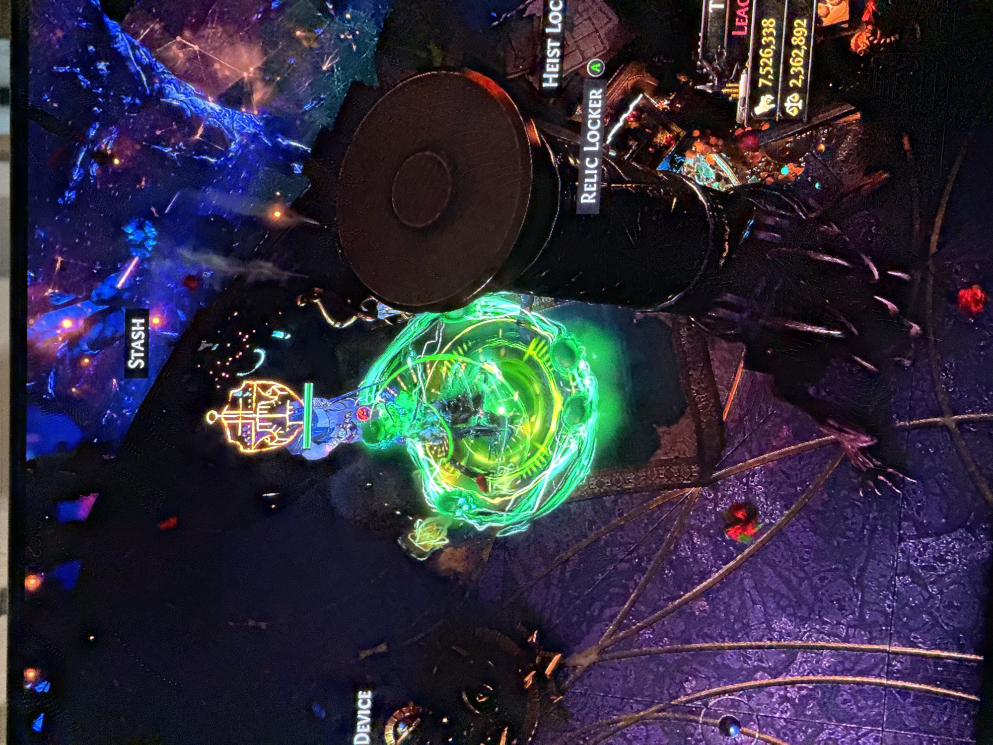 The image shows a screen capture of a video game, likely taken from a television or monitor. In the game, there are in-game interfaces, various objects, and a character amidst a fantastical, digitally rendered environment. The scene shows a "Stash", a "Relic Locker", and a "Crafting Device", the context suggesting they are interactive elements within the game. In the top right corner of the screen are game statistics: "7,526,338" and "2,362,892", likely currency or points. The environment seems to be abstract, with an emphasis on dark shades, purple, and blue, and includes elements like a web pattern on the ground.
The location is impossible to determine as it is a fantasy game.