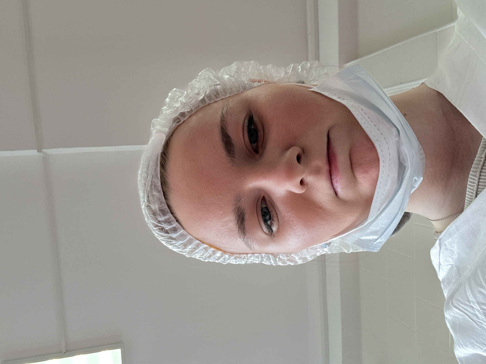 The image depicts a person, likely a medical professional, wearing a surgical cap and mask, partially lowered on their face, suggesting a healthcare setting. The individual's face is the primary focus, with a neutral expression. The background features a ceiling with fluorescent lighting, consistent with hospital or clinic interiors. The location is specified as Unknown, Russia.