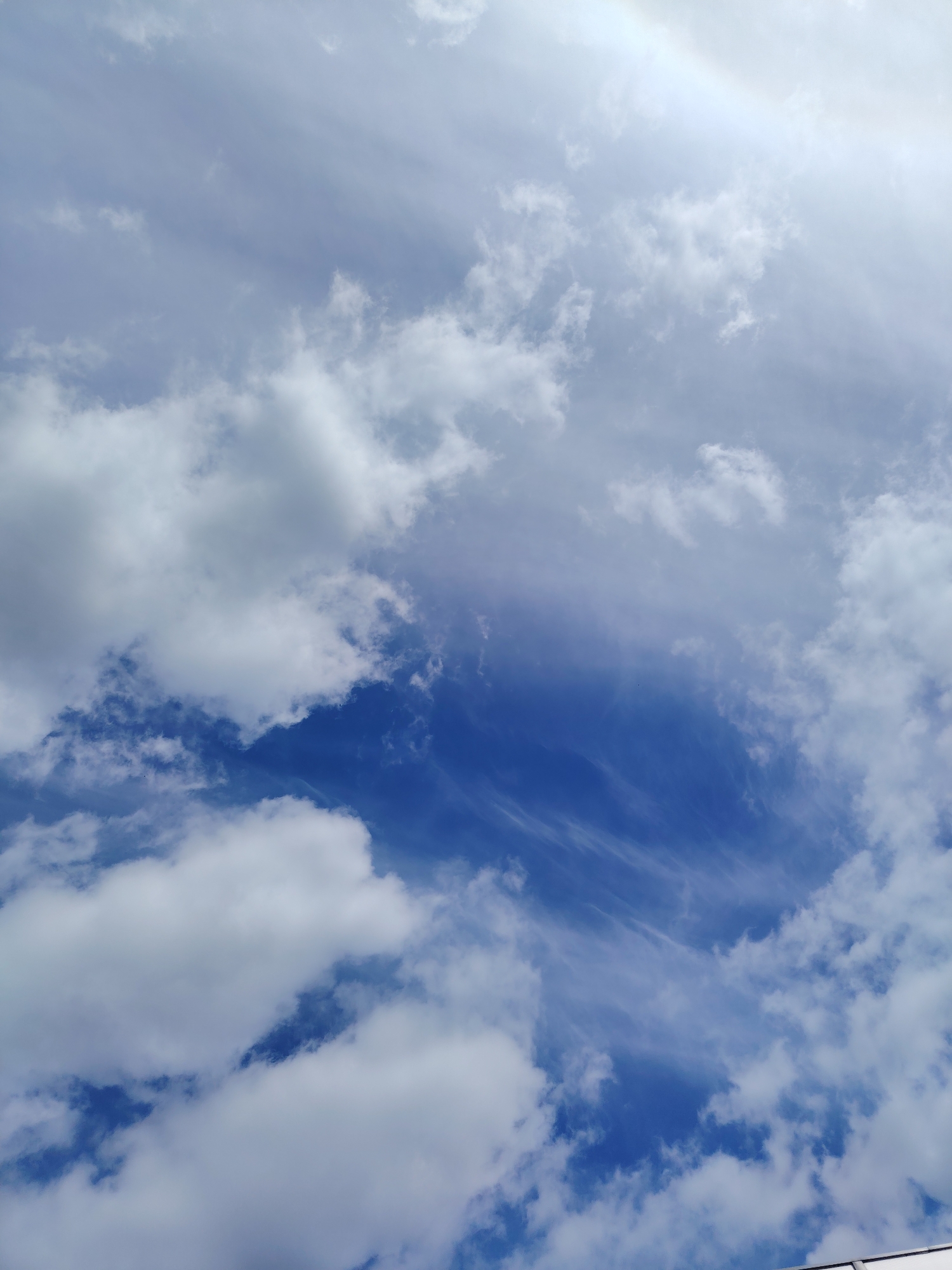 This is a photograph of a blue sky filled with various types of clouds. In the foreground, there are fluffy, white cumulus clouds. Further back, there are thinner, wispy cirrus clouds that stretch across the sky. The overall impression is of a bright, somewhat overcast day. The image does not depict any structures, people, or specific urban features that would indicate a location within the city of Хоругвино, Russia, or any other city. The image is a natural landscape scene.