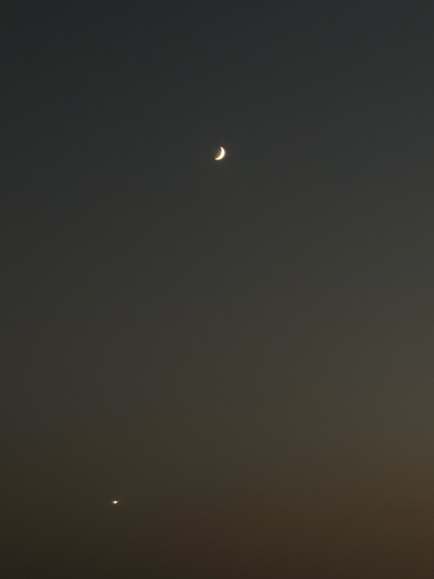 The image shows a dark sky with a sliver of the crescent moon visible in the upper right quadrant. In the lower left quadrant, a small, bright celestial body, likely a planet, is visible. The sky appears to be twilight or nighttime. There are no people, buildings, or other elements of a city visible in the frame. The image composition is focused on the celestial objects against a dark backdrop. There is no specific information in the image that indicates the location of Sharm El Sheikh, Egypt.