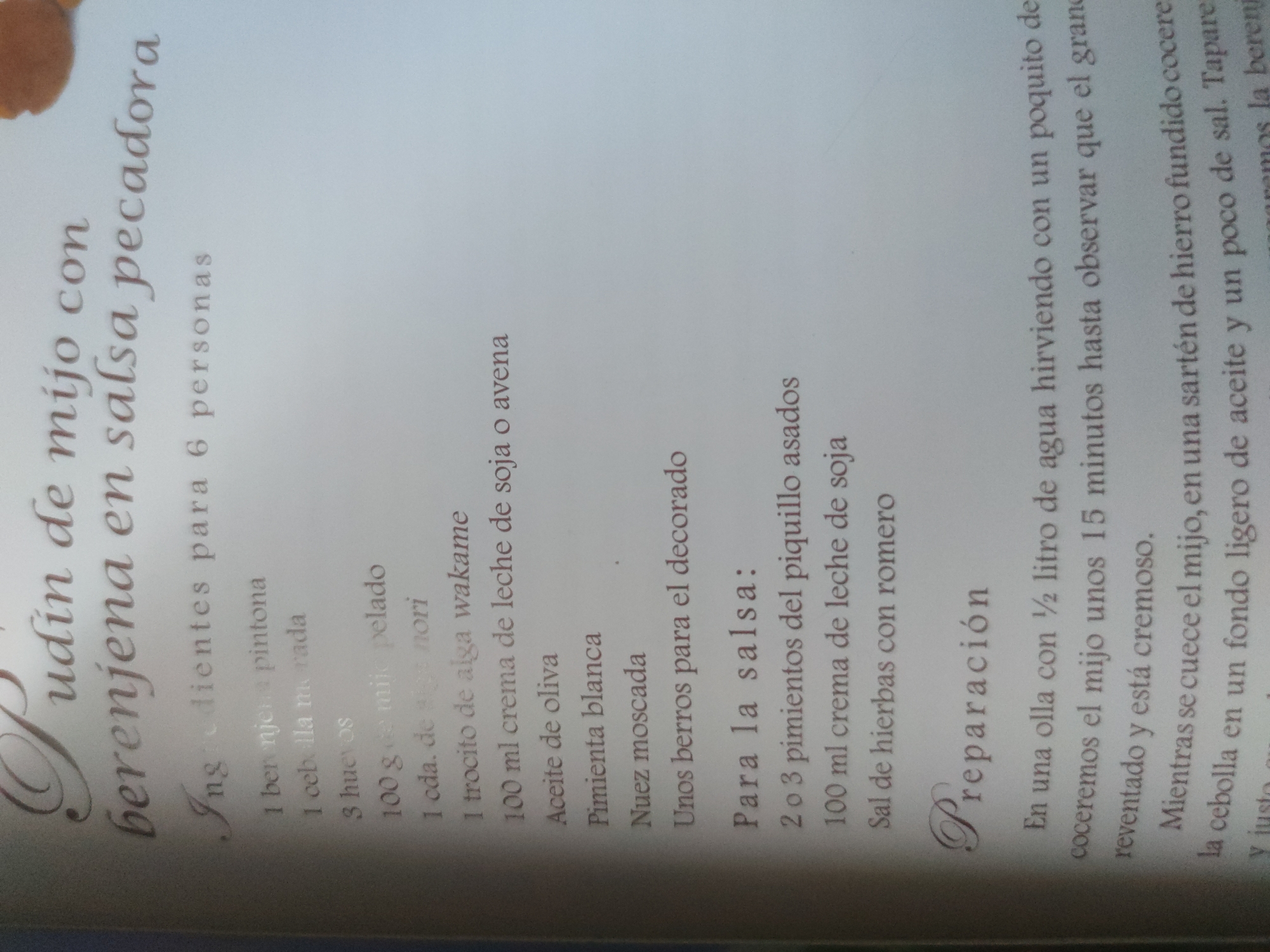 The image is a close-up shot of a recipe, likely from a cookbook. The title reads "Pudin de mijo con berenjena en salsa pecadora," which translates to "Millet Pudding with Eggplant in Sinful Sauce." Below the title, it states that the recipe serves 6 people.
The recipe lists the ingredients: one "pintona" eggplant, one red onion, 3 eggs, 100g peeled millet, 1 tbsp nori seaweed, 1 piece of wakame seaweed, 100 ml soy or oat milk cream, olive oil, white pepper, nutmeg, and watercress for decoration.
A separate ingredient list follows for the sauce: 2 or 3 roasted piquillo peppers, 100 ml soy milk cream, and herbal salt with rosemary.
Below the ingredients is the heading "Preparación" (Preparation). The instructions indicate boiling millet in ½ liter of water with a little salt for 15 minutes until expanded and creamy. Meanwhile, cook the chopped onion in a light amount of oil and salt in an iron skillet until ready. Then, add the eggplant.