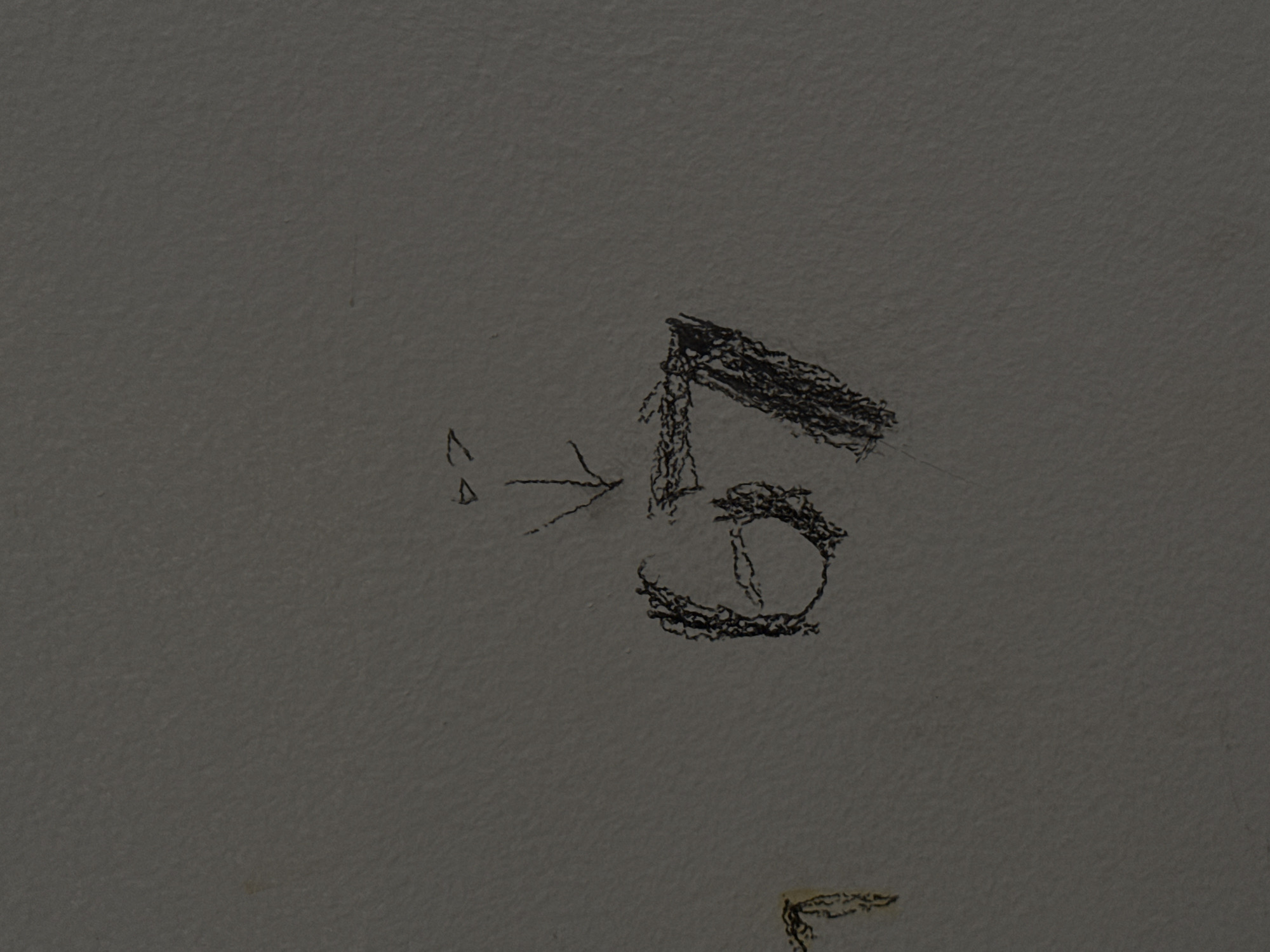 The image shows a close-up, eye-level, medium shot of a light gray, textured wall. There are two markings on the wall. To the left, a faint, yellow marking that appears to be part of a letter or symbol is visible. To the right, a sketch in black crayon depicts the number "67" with a line and arrowhead above it, pointing downwards. The wall is likely a surface in an interior or exterior space. There are no people or other objects clearly depicted in the scene. The scene appears to be static and devoid of immediate action. The lighting is even, suggesting ambient light without any strong directional sources.