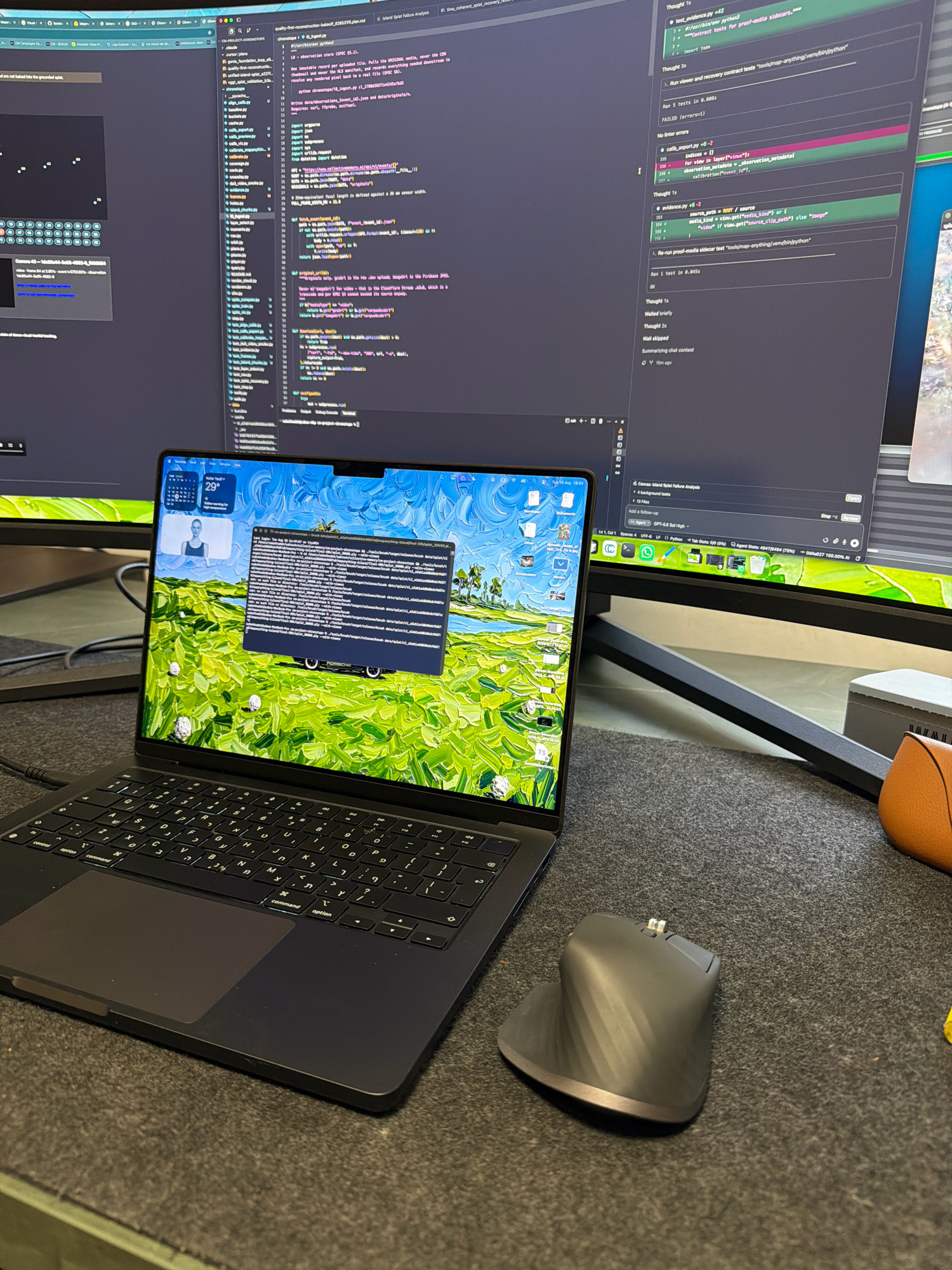 The image depicts a modern workspace with two large computer monitors and a laptop. The laptop is open and displays a terminal window with lines of code and file paths. The wallpaper on the laptop's desktop is a vibrant, impressionistic painting of a landscape with a body of water. A vertical mouse sits to the right of the laptop. The background monitors also display code and graphical interfaces. The overall setting suggests a professional environment, likely for software development or data analysis. The scene is captured from a slightly elevated perspective, focusing on the desk area. There are no visible people in the image. The location is not explicitly shown or identifiable as Kafr Yasif, Israel.