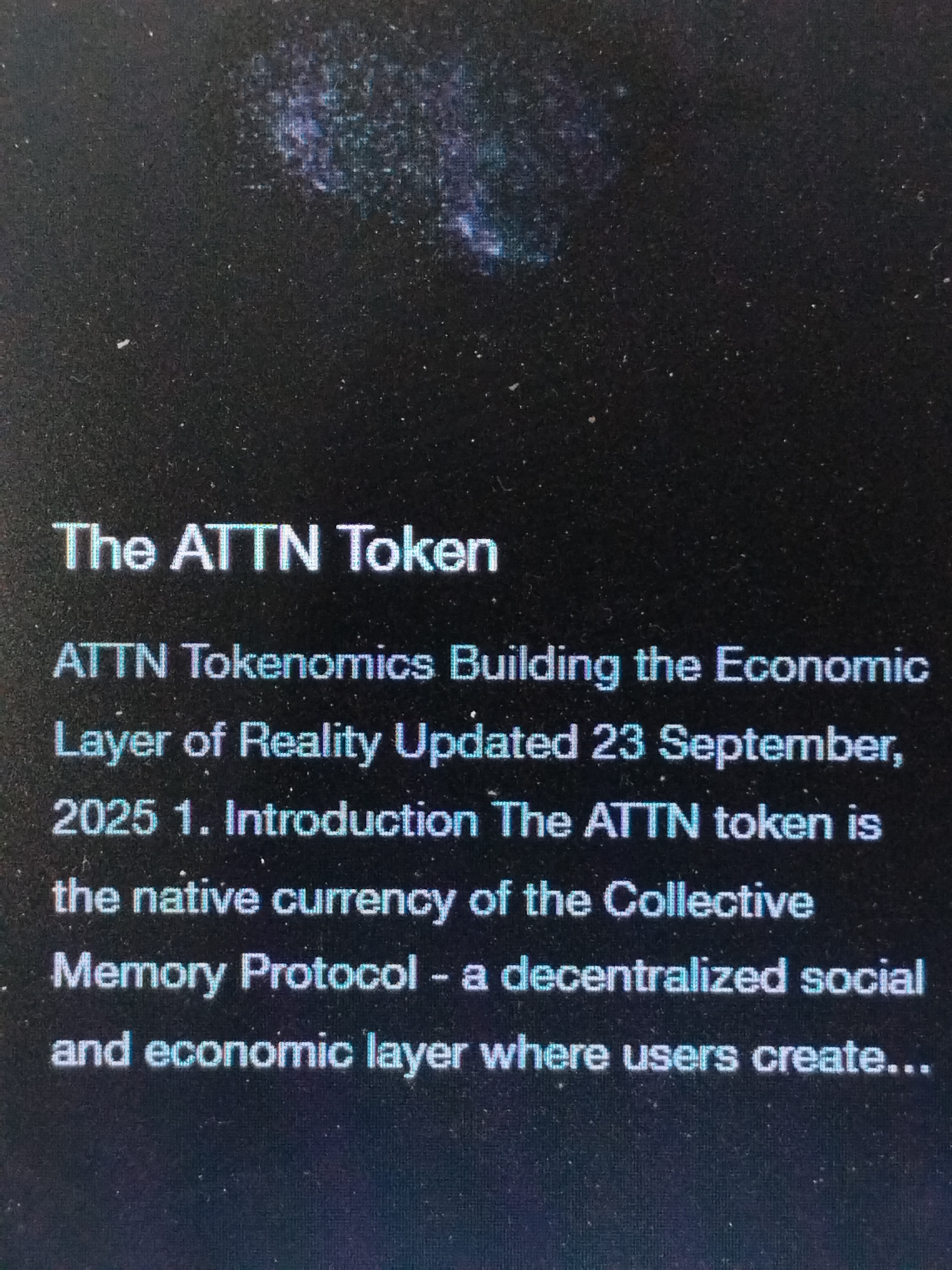 The image displays text against a dark background, possibly a screen or a printed document. The text includes the title "The ATTN Token," followed by descriptive lines about ATTN Tokenomics building the Economic Layer of Reality and mentions an update date of 23 September, 2025. The text further describes the ATTN token as the native currency of the Collective Memory Protocol, which is defined as a decentralized social and economic layer where users create. A blurry, dark pattern fills the upper portion of the image. There is no information related to a location in Lhokseumawe, Indonesia, present in the image.