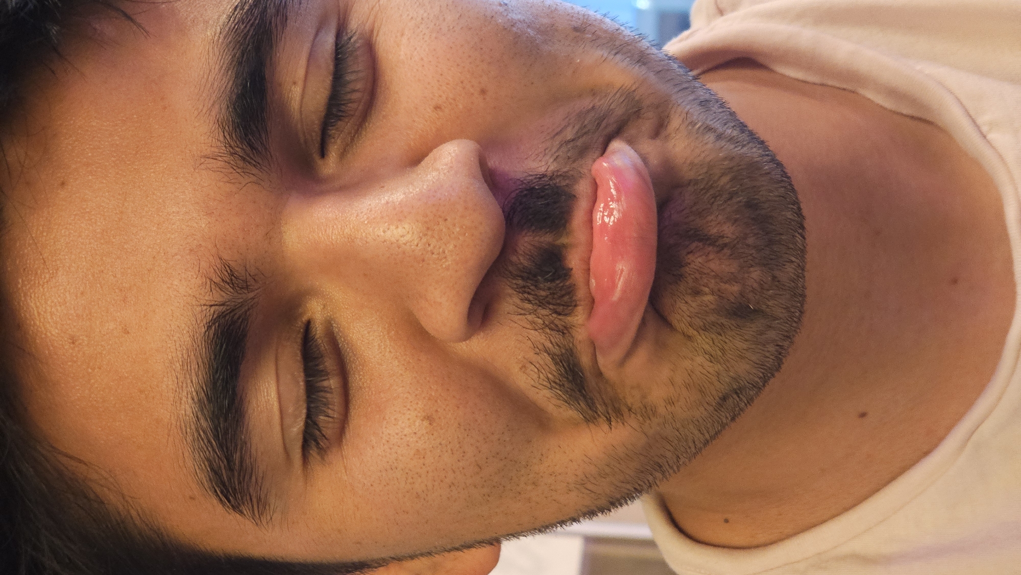 A close-up, rotated portrait depicts a man with closed eyes, a beard, and his tongue protruding from his mouth. He is wearing a light-colored shirt. The setting or location in Puebla, Mexico is not identifiable from the image.