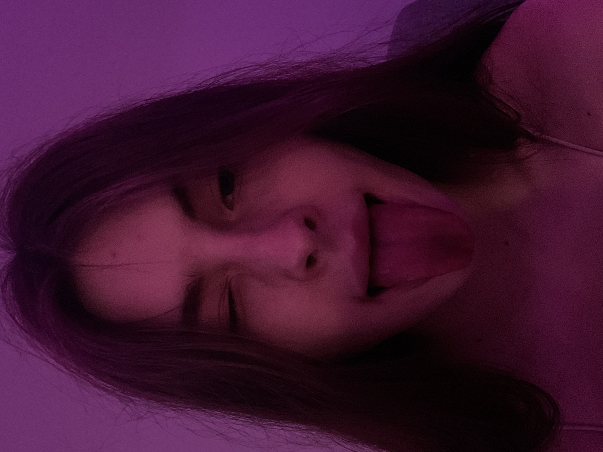 A close-up, tilted shot features a young woman with dark hair sticking out her tongue. The lighting appears to be predominantly purple. The image does not contain enough information to discern a location, specifically Saint Petersburg, Russia.