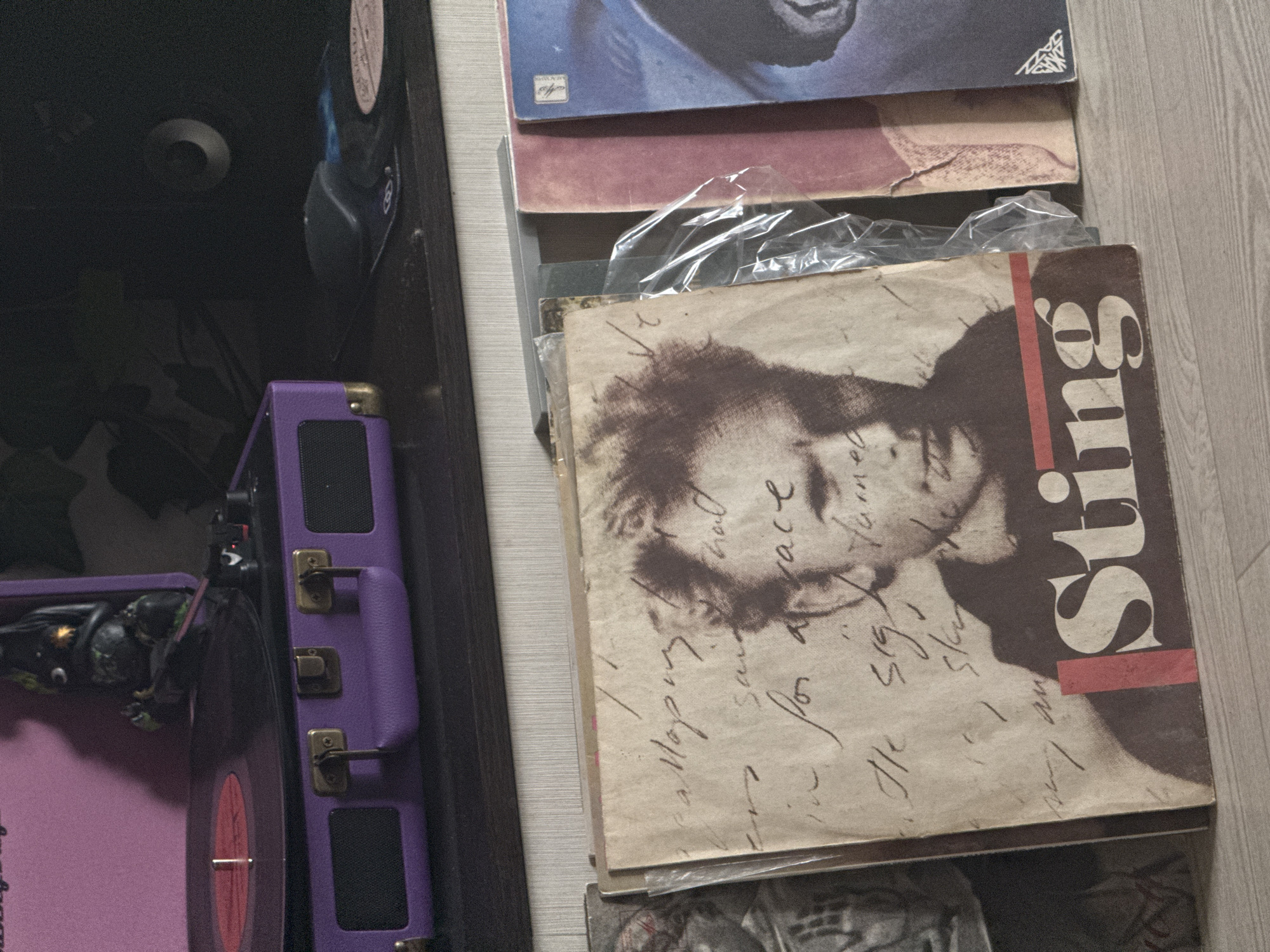 The image shows a stack of vinyl records next to a purple record player. The record on top is Sting's "...Nothing Like the Sun." The image does not show anything that would indicate it was taken in Novo-Nikol'skoe, Russia.