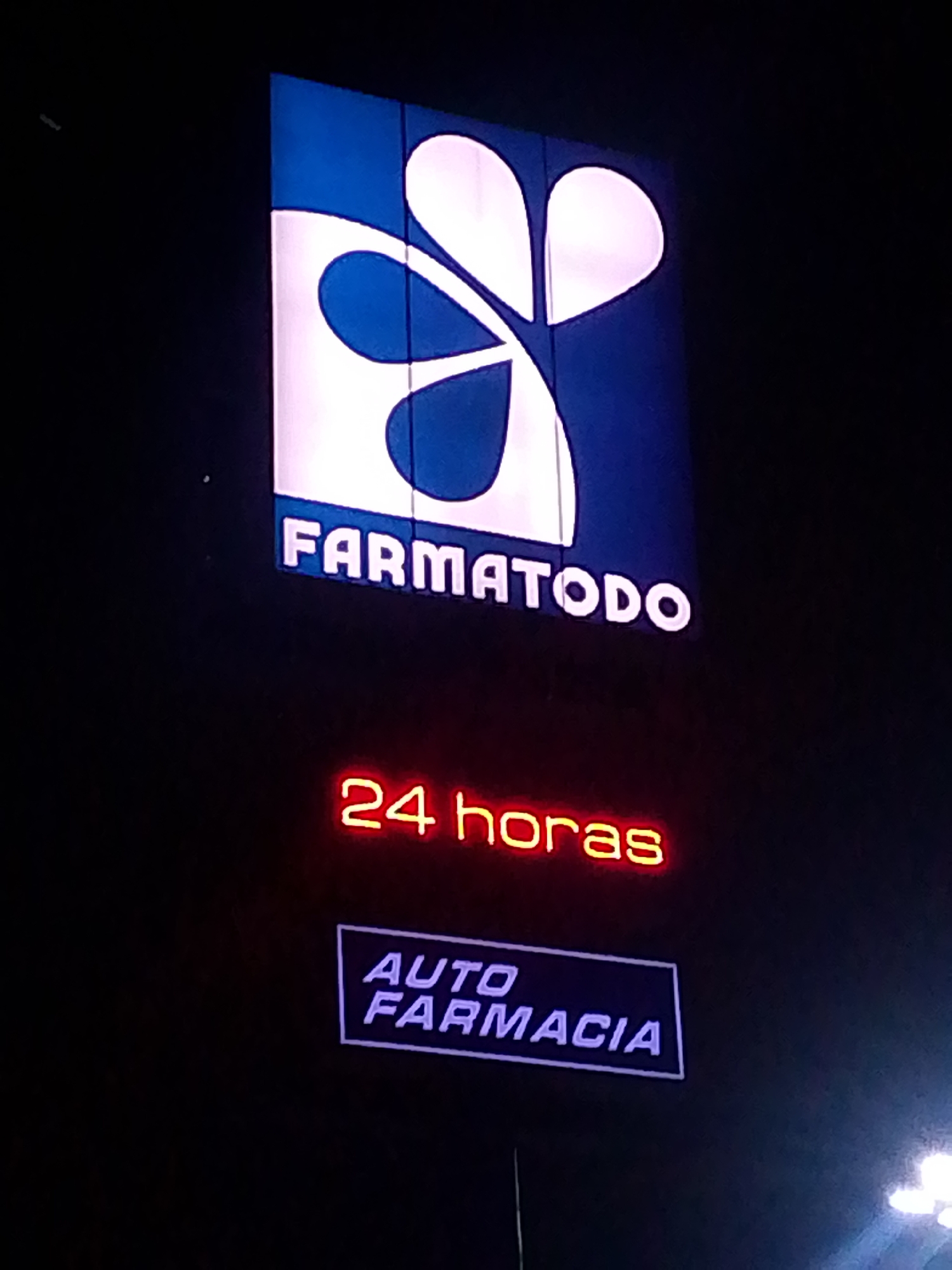 The image shows the sign of a Farmatodo store, indicating it's open 24 hours and has an auto-pharmacy. The location appears to be at night in an unknown city.