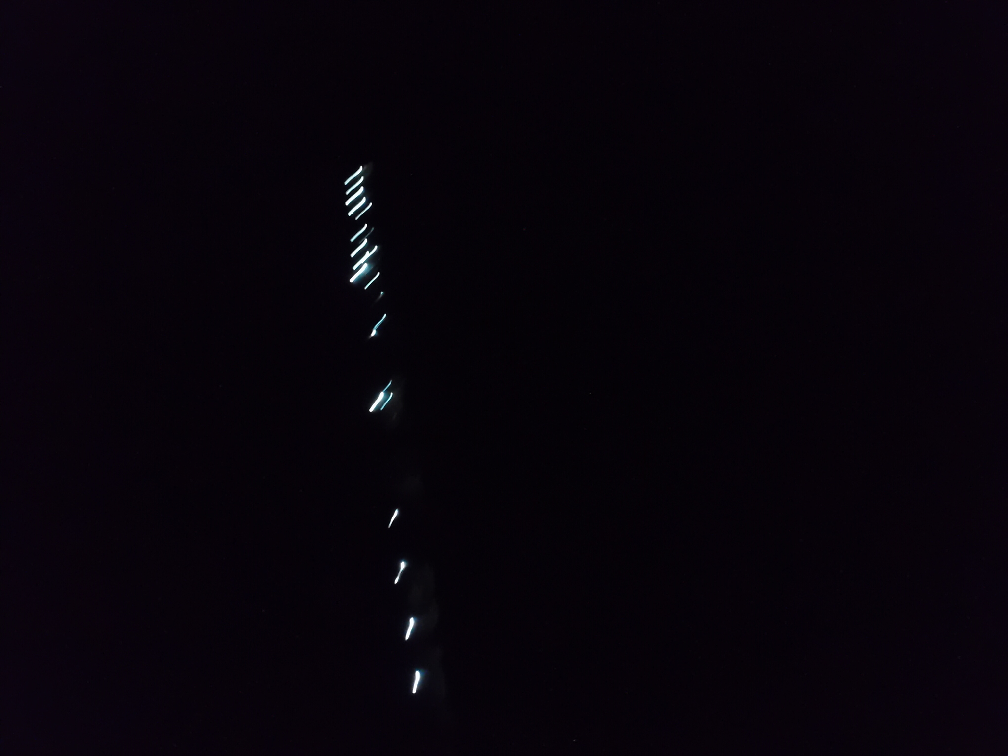 The image captures a long exposure shot of lights in the dark. Several streaks of white and light blue light are visible across the frame, suggesting movement of light sources. The lights appear to be arranged in a scattered, linear fashion. The background is entirely black, indicating a nighttime scene with minimal ambient light. The specific location in Jauro Yinu, Nigeria, is not visually discernible from the image itself; the context of the location is provided externally. No people or specific objects are clearly identifiable beyond the light streaks.