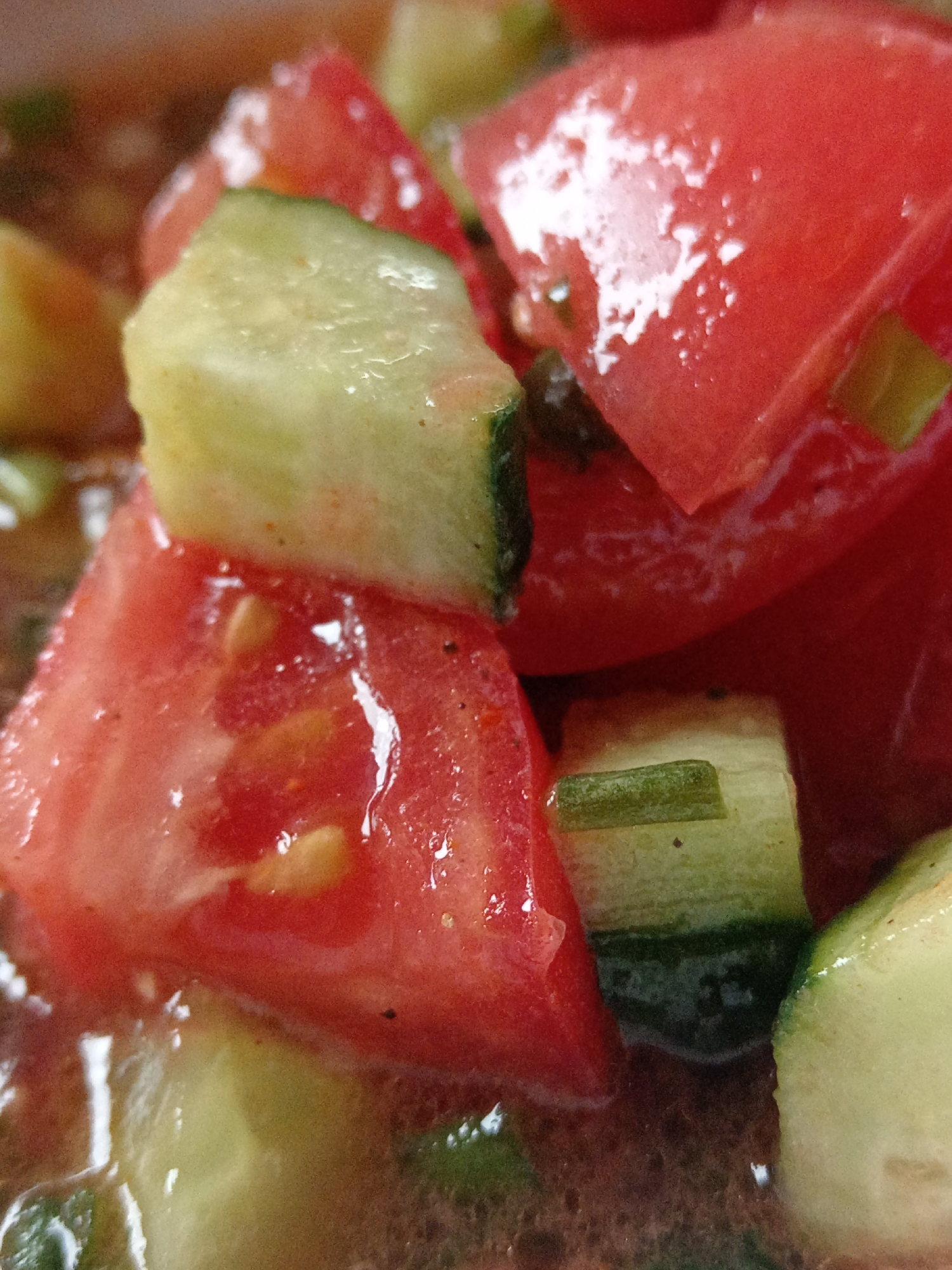 A close-up, overhead shot captures a bowl of gazpacho, a cold soup made with blended vegetables. The soup is composed of chopped tomatoes, cucumbers, and possibly other red and green ingredients, all immersed in a reddish liquid. The scene is lit by overhead lighting, causing reflections on the wet surfaces of the vegetables. The image focuses on the texture and vibrant colors of the ingredients. The location is specified as Uchkeken, Russia. There are no people or visible actions occurring in the image.