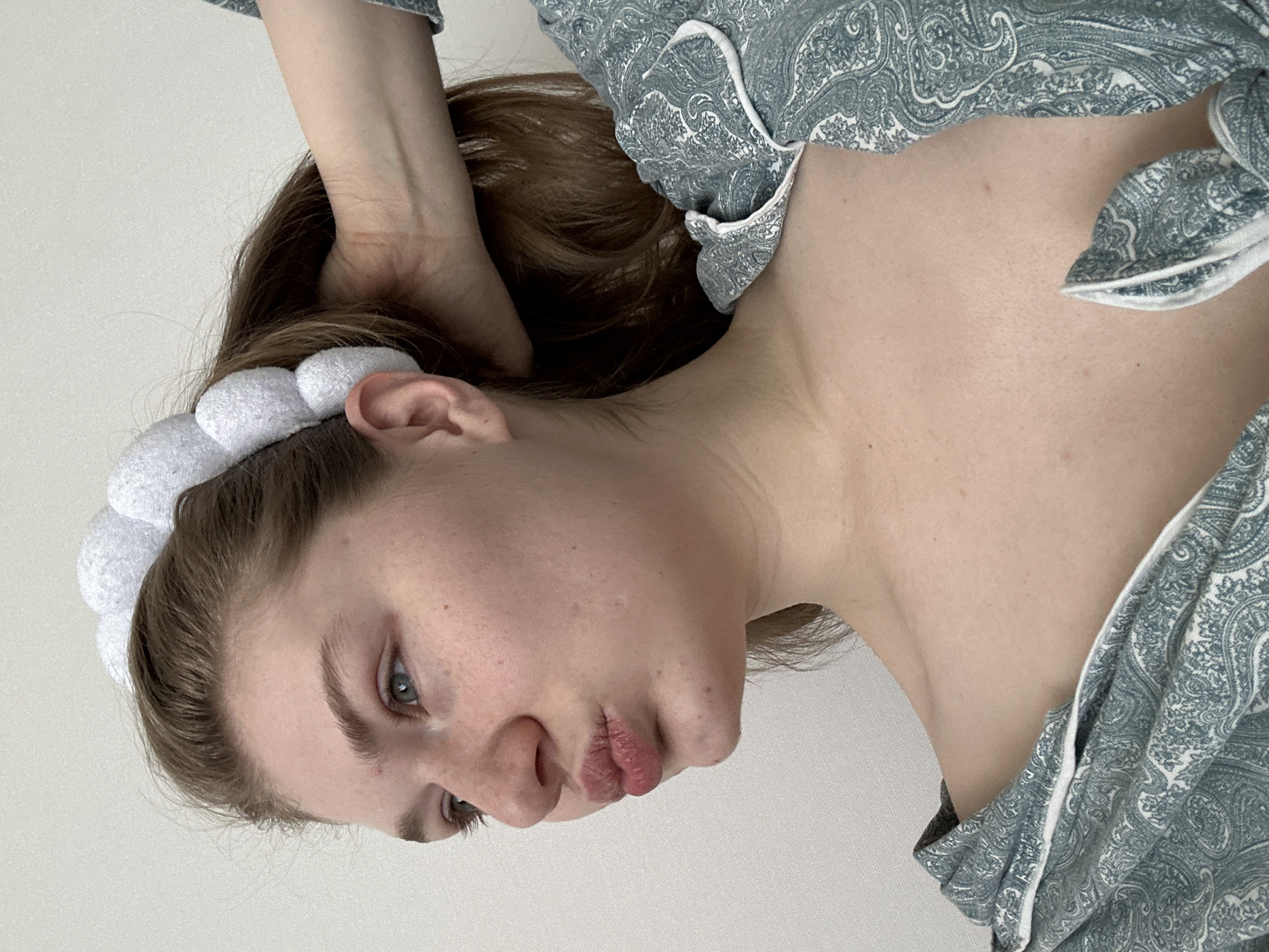 A young woman wearing a white headband and a patterned pajama top is lying on a white surface. She has her hand behind her head. The location is unknown, and there is no information available to suggest the image was taken in Kazan, Russia.