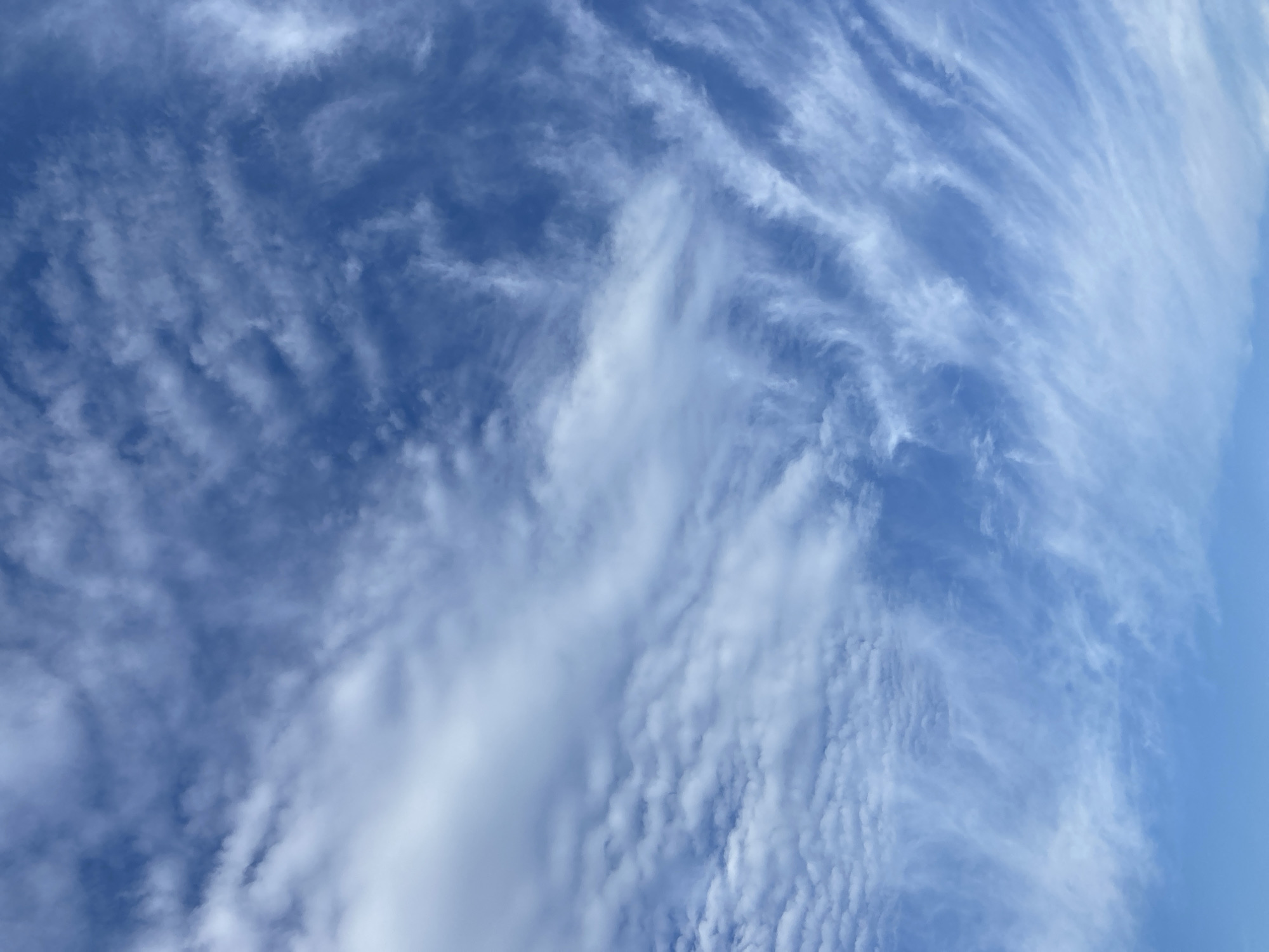 A clear, blue sky is filled with wispy, white cirrus clouds. The clouds are scattered and appear to be moving from left to right across the frame. The lower portion of the image shows a gradient of blue, becoming lighter towards the bottom.