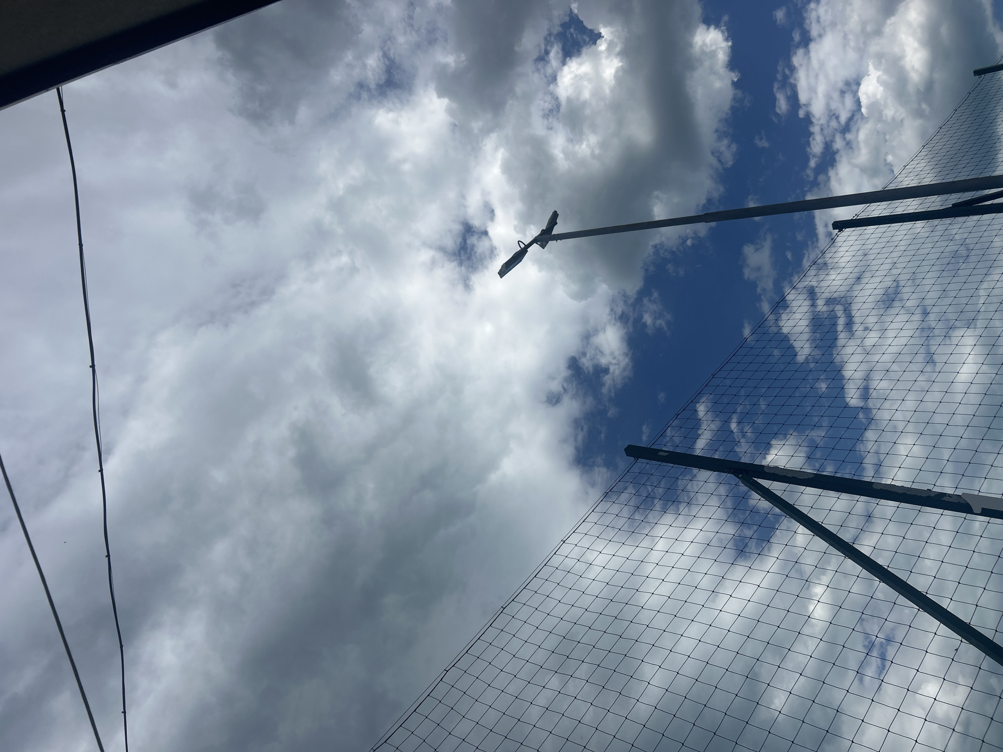 The image, taken from a low angle, shows a sky with a mix of dark and light clouds. A security light mounted on a pole is visible against the sky. A chain-link fence is also in the frame. The location appears to be in Varna, Bulgaria.