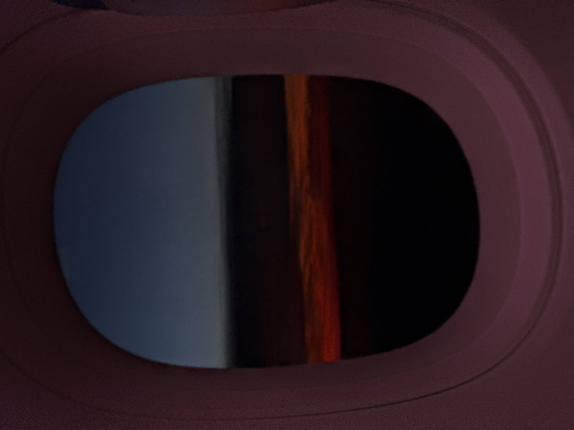 The image depicts a view from what appears to be an airplane window. Outside the window, there is a dark area, with some gray/blue and orange streaks to the side. The window frame has a layered, oval shape, with colors of purple and pink. I have no information about Sofia, Bulgaria.
