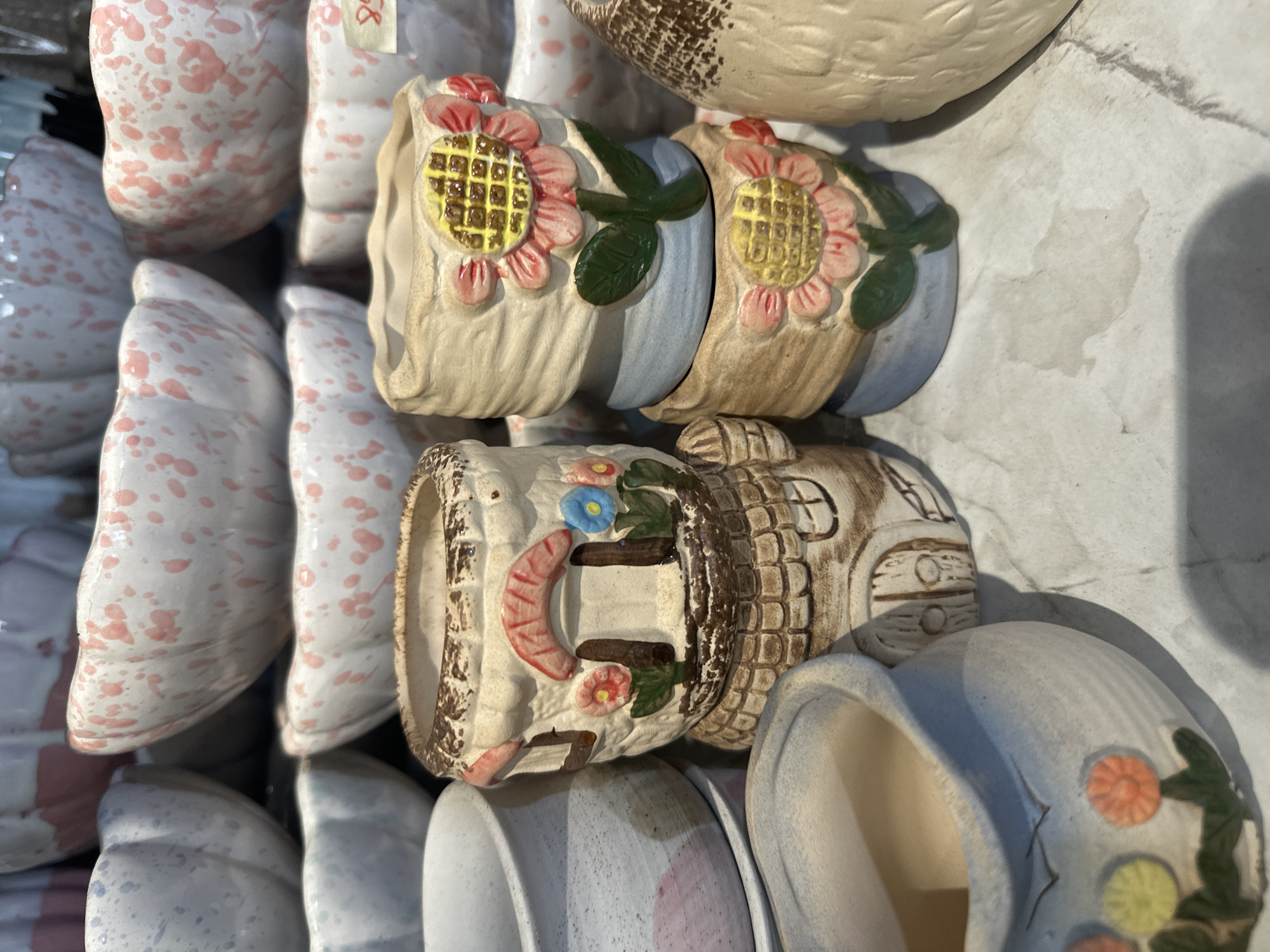 The image shows a collection of small, decorative ceramic pots, likely for plants. The pots are various shapes and sizes with different painted designs, including flowers and a house. The pots appear to be arranged on a flat surface, possibly for sale. There is no clear indication of the location being in Bac Nha Trang Ward, Vietnam; this information cannot be verified from the image alone. The scene contains no people and the primary focus is on the presentation of the ceramic pots.