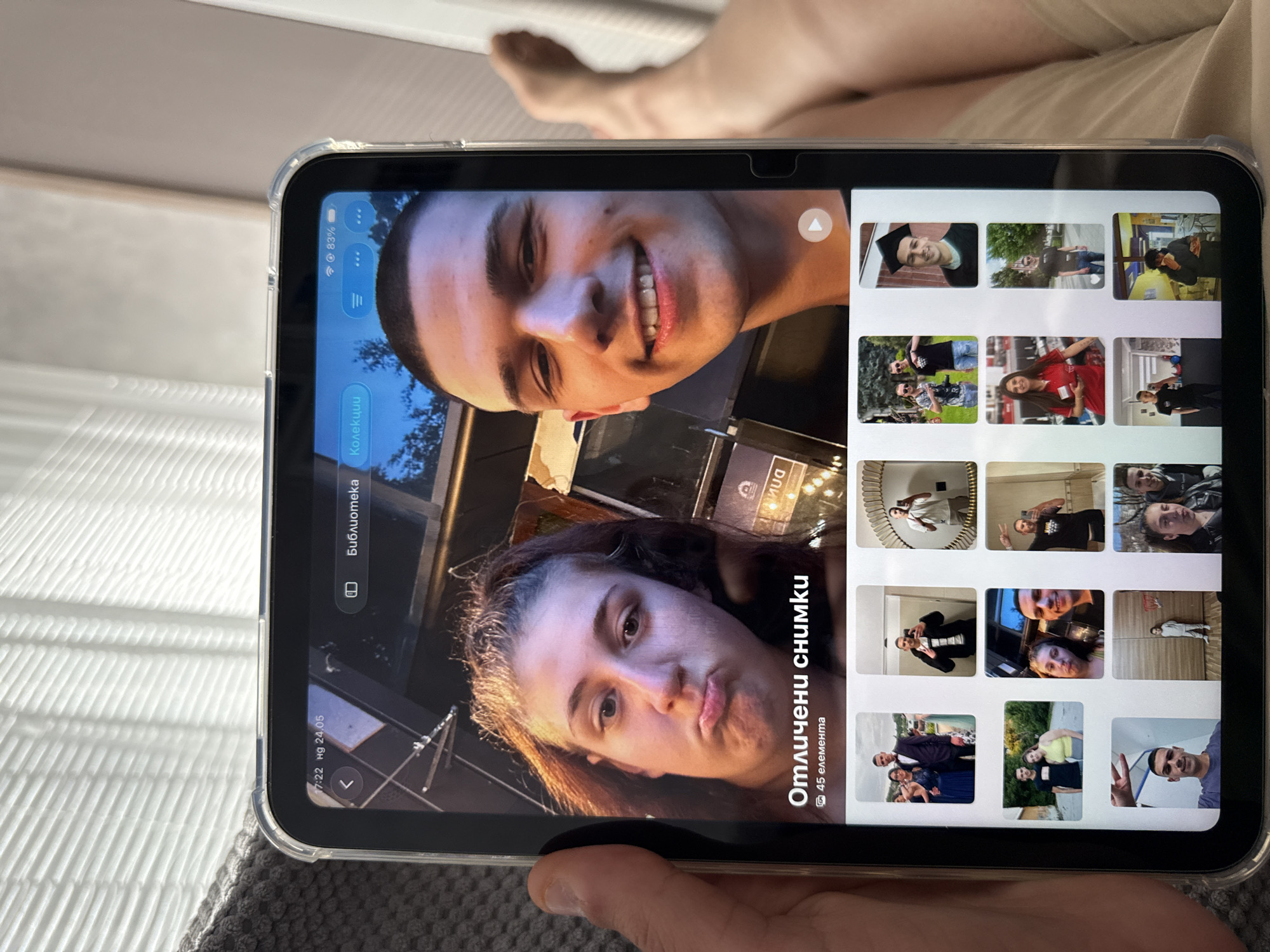A person is holding a tablet showing a photo of a man and a woman. The tablet screen also displays thumbnail photos. The tablet reads "Отличени снимки 45 елемента" meaning "Featured photos 45 elements", and "Библиотека". The time displayed on the tablet is 17:22 на 24.05. The screen indicates 83% battery life. A human leg and foot are visible in the background, suggesting the scene is indoors. The image does not provide sufficient information to determine the location in Lovech, Bulgaria.