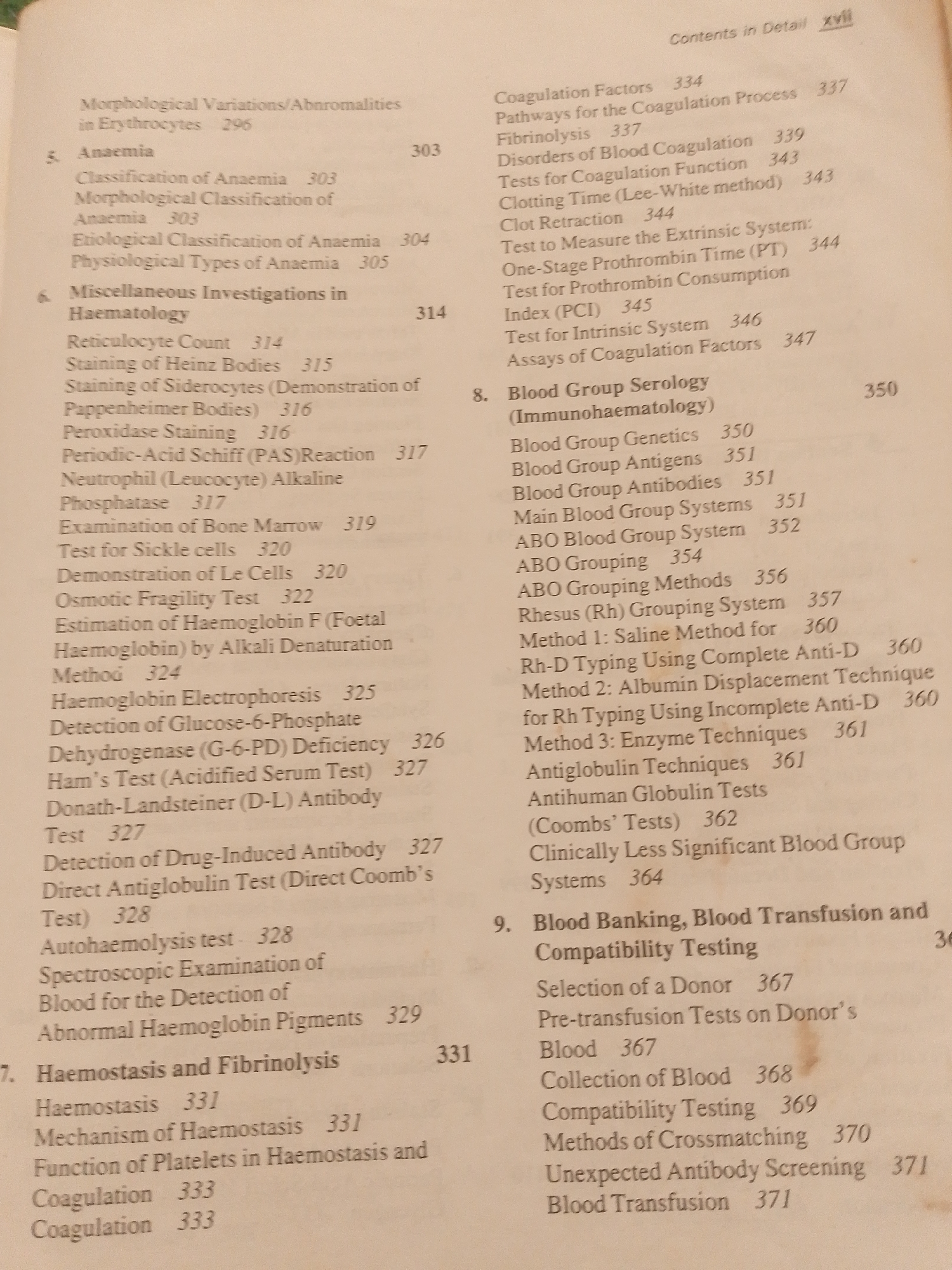 The image is a scanned page from a textbook, likely a medical or biological science publication, containing a detailed table of contents. The page is laid out in a typical textbook format with numbered sections and sub-sections, each accompanied by corresponding page numbers. The text is primarily in black ink on a light-colored background, suggesting it is a printed document.
The content of the table of contents focuses on hematology and blood-related topics. It includes sections such as "Anaemia," "Miscellaneous Investigations in Haematology," "Haemostasis and Fibrinolysis," "Blood Group Serology (Immunohaematology)," and "Blood Banking, Blood Transfusion and Compatibility Testing." Specific entries detail various tests, classifications, mechanisms, and techniques related to these subjects, like "Reticulocyte Count," "Staining of Heinz Bodies," "Coagulation Factors," "Rhesus (Rh) Grouping System," and "Methods of Crossmatching."
At the top right corner, the text "Contents in Detail xvii" indicates this is a detailed table of contents for a section or chapter, with "xvii" likely representing the page number within that detailed section. The overall presentation is academic and informational, devoid of any imagery of people, specific objects, or a particular scene beyond the context of a printed document. The environment is implied to be a library, study, or office where such a book would be kept. There are no cues about time of day, weather, or emotions, as it is a purely textual representation of information. The location context "Jauro Yinu, Nigeria" is not directly evident from the visual content of the page itself, but is provided as external information.