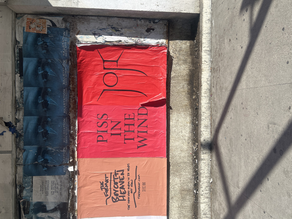 A collection of posters is adhered to a concrete wall. One poster, in red, features the phrase "PISS IN THE WIND" below an abstract symbol. Another, in orange, promotes "THE FORMAT BOYCOTT HEAVEN," advertising "THE FIRST NEW ALBUM IN 22 YEARS." A third poster, visible in fragments, includes "KILL STATION DAYS AFTER DYING." On the left, a faded advertisement mentions "SENESCENCE" and a performance at "THE HILTERN SATURDAY 07.20.24." A "DUMPER FOCKFACE" sticker is affixed above.