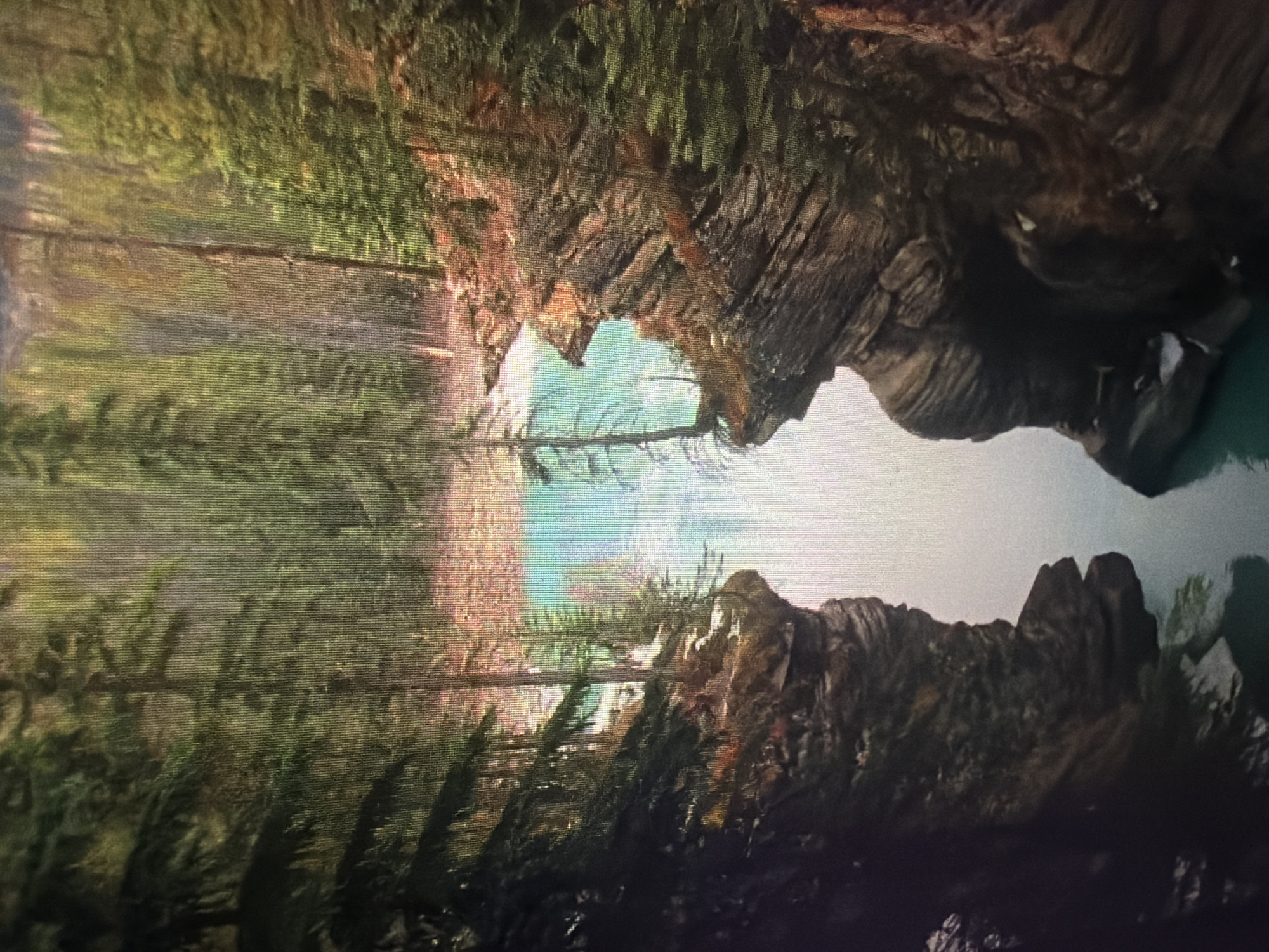 The image shows a natural scene with a turquoise river flowing between rocky cliffs covered in trees. The water is calm, and the surrounding forest is dense with tall evergreens. The rocks are layered and appear to be eroded by water over time. There are no people or man-made structures visible in the scene. The lighting suggests it might be daytime, possibly with some overcast conditions as there are no strong shadows. The scene is likely a wilderness area, possibly a gorge or canyon, focused on the natural beauty of the landscape. The location is not in Baan Mae Nam, Thailand, as the environment depicted is not characteristic of that region.