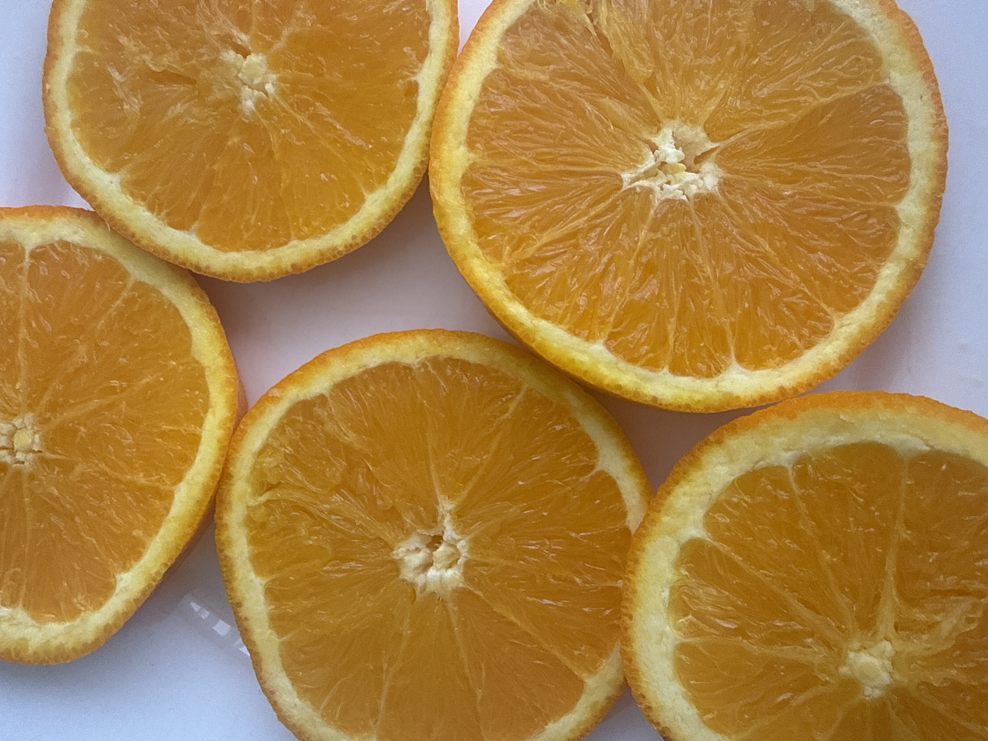 The image shows five slices of oranges arranged on a white surface. The orange slices are cut in a circular shape, with the characteristic orange segments visible within each slice. The color of the oranges ranges from a bright orange to a slightly more yellowish-orange. The rind around the edges of the slices is light yellow. The background is plain white. There are no indications about the location being in Alanya, Turkey, or any other details about people, subjects, or interactions within the image.