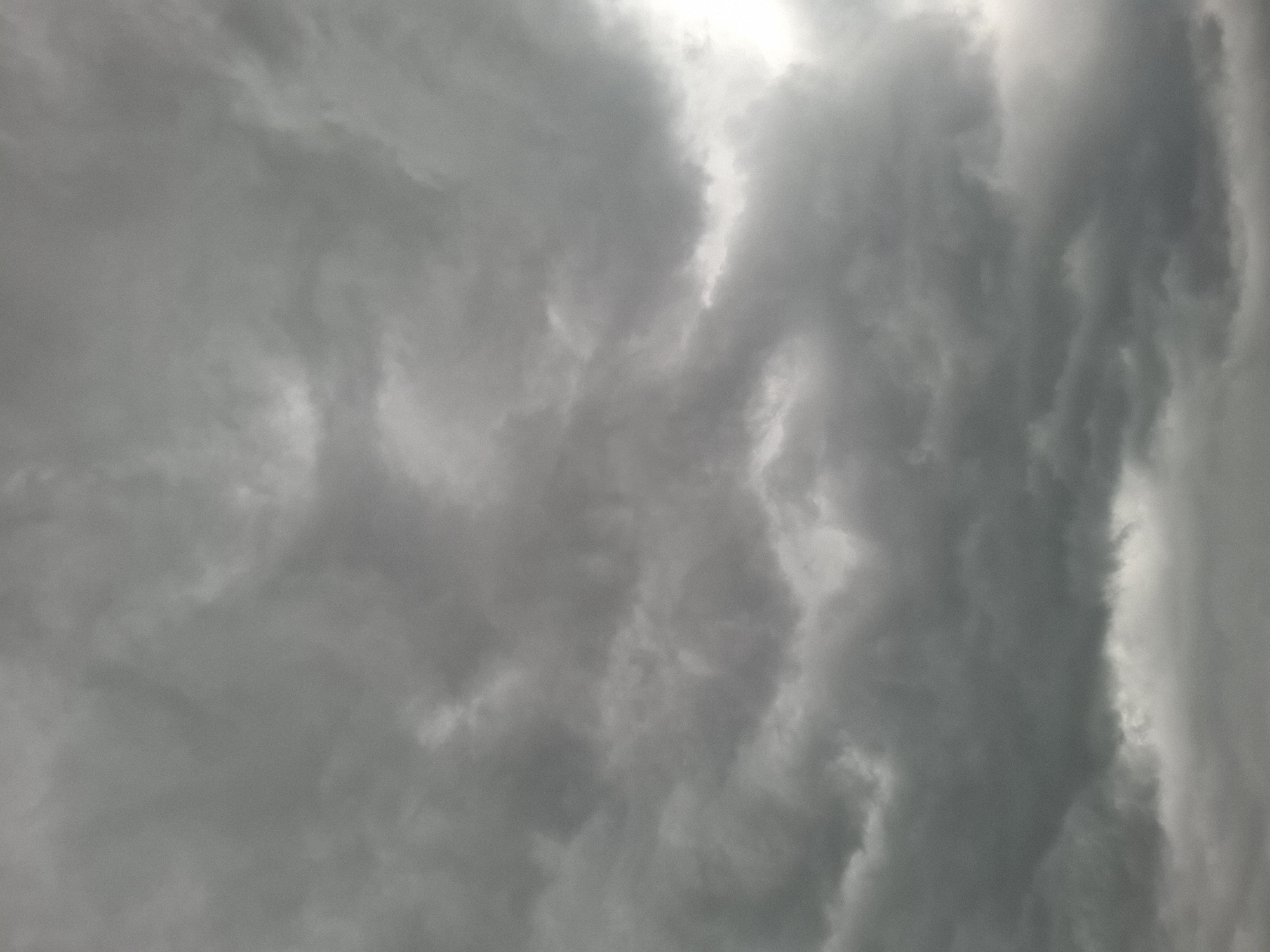 The image shows a sky filled with dark, heavy storm clouds. The clouds are swirling and textured, with varying shades of gray. Sunlight is partially visible through gaps in the clouds. The image was supposedly taken in Khlevnoye, Russia, but there's nothing in the image itself to confirm this location. There are no visible people, subjects, objects, actions, or interactions in the image other than the clouds and light. The environment is strictly atmospheric.