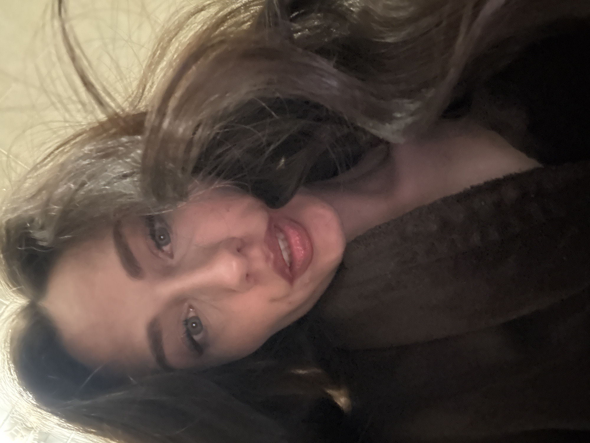 A close-up, angled portrait of a young woman with long, brown hair. She has fair skin, light-colored eyes, and slightly parted lips. She appears to be wearing a dark-colored, possibly fur, garment. The background is a blurry, light beige color. The angle suggests the photo was taken from above, looking down at the woman. There is no information about the location being Saint Petersburg, Russia.