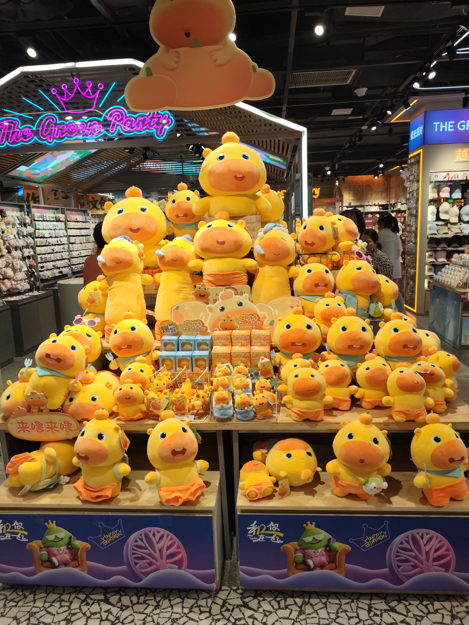 This image depicts a retail display of yellow duck plush toys in a store, likely in Daqing, China, given the presence of Chinese text on signage and packaging. The display is elaborate, featuring multiple tiers of plush toys in various sizes and poses. Some are large, standalone figures, while others are arranged in smaller groups or displayed with accessories like forks and sunglasses. The background reveals more shelves stocked with merchandise and overhead store lighting. The overall impression is one of a vibrant, commercial setting with a focus on novelty or children's products.