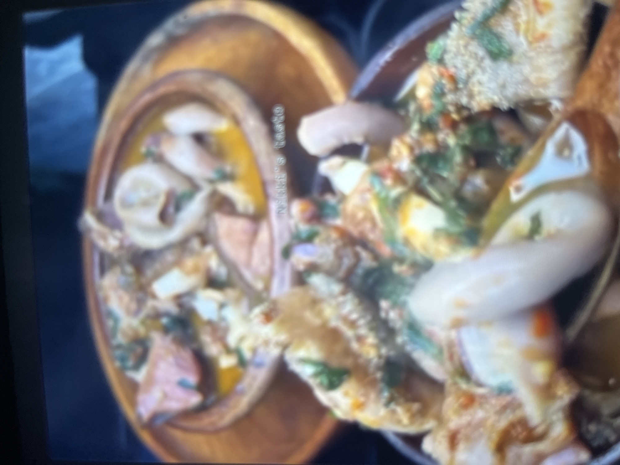The image shows two bowls of a traditional Nigerian dish, likely assorted meat pepper soup, a delicacy common in Abuja, Nigeria. The dish appears to be made with various types of meat and offal, seasoned with local spices and herbs, giving it a rich, flavorful appearance. The bowls are placed on a wooden surface, suggesting a casual dining setting, possibly at a restaurant or home. The lighting is dim, and the image is slightly blurred, which gives it a warm, inviting feel. The dish is a popular choice for those seeking authentic Nigerian cuisine, and its presence in the image points to a culinary experience that reflects the local culture and traditions of Abuja.