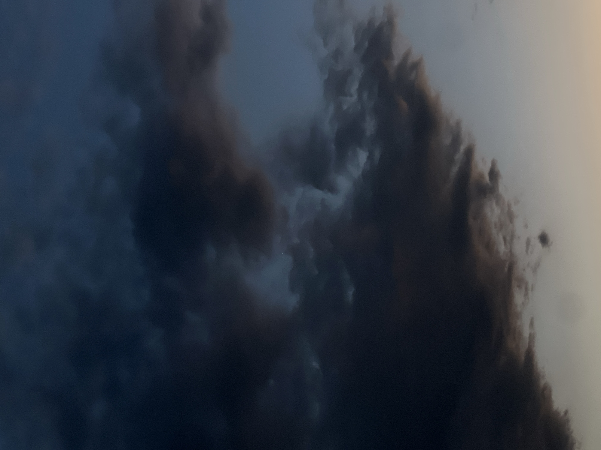 The image depicts a dramatic sky filled with dark, ominous clouds. The clouds are dense and textured, ranging in color from deep charcoal to lighter grays, with hints of a pale orange or yellow at the very bottom, suggesting either the setting or rising sun. The sky itself transitions from a dark, stormy blue in the upper portion to a lighter, clearer sky towards the bottom. There are no visible signs of human presence, structures, or any recognizable landmarks that would indicate a specific location within the city of Plovdiv, Bulgaria. The scene is purely focused on the atmospheric conditions of the sky.