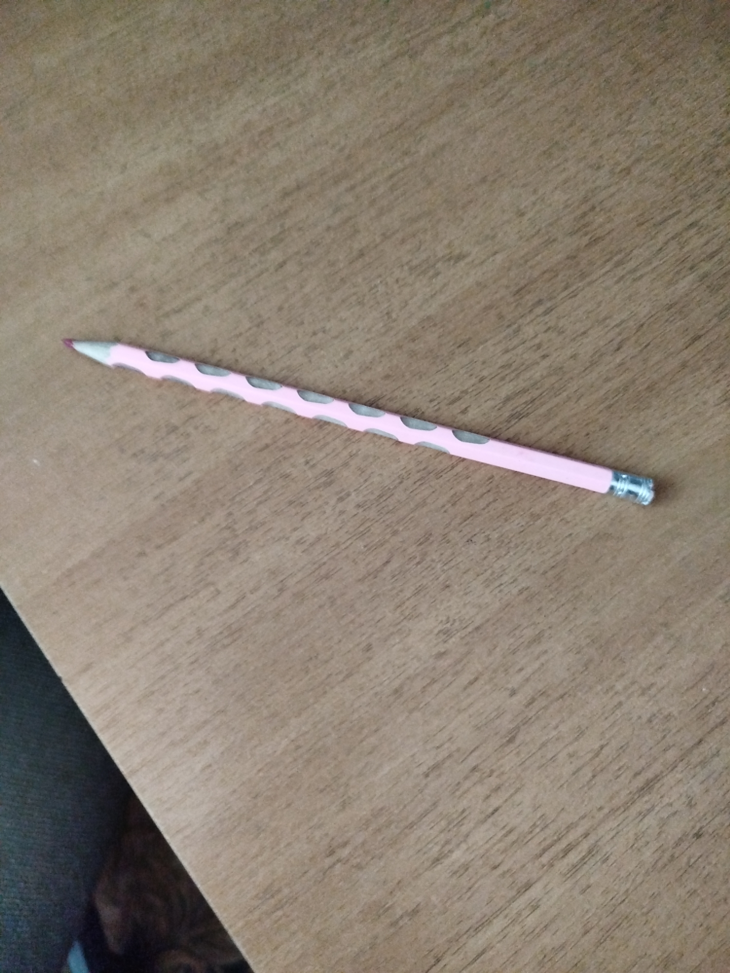A pink pencil with gray polka dots lies diagonally on a wooden surface. The pencil has a sharpened tip and a metal eraser holder at the opposite end. The wooden surface appears to be a table or desk with visible grain patterns. The lighting suggests an indoor setting. The location in Крывасельскі сельскі Савет, Belarus, is not evident from the image itself.