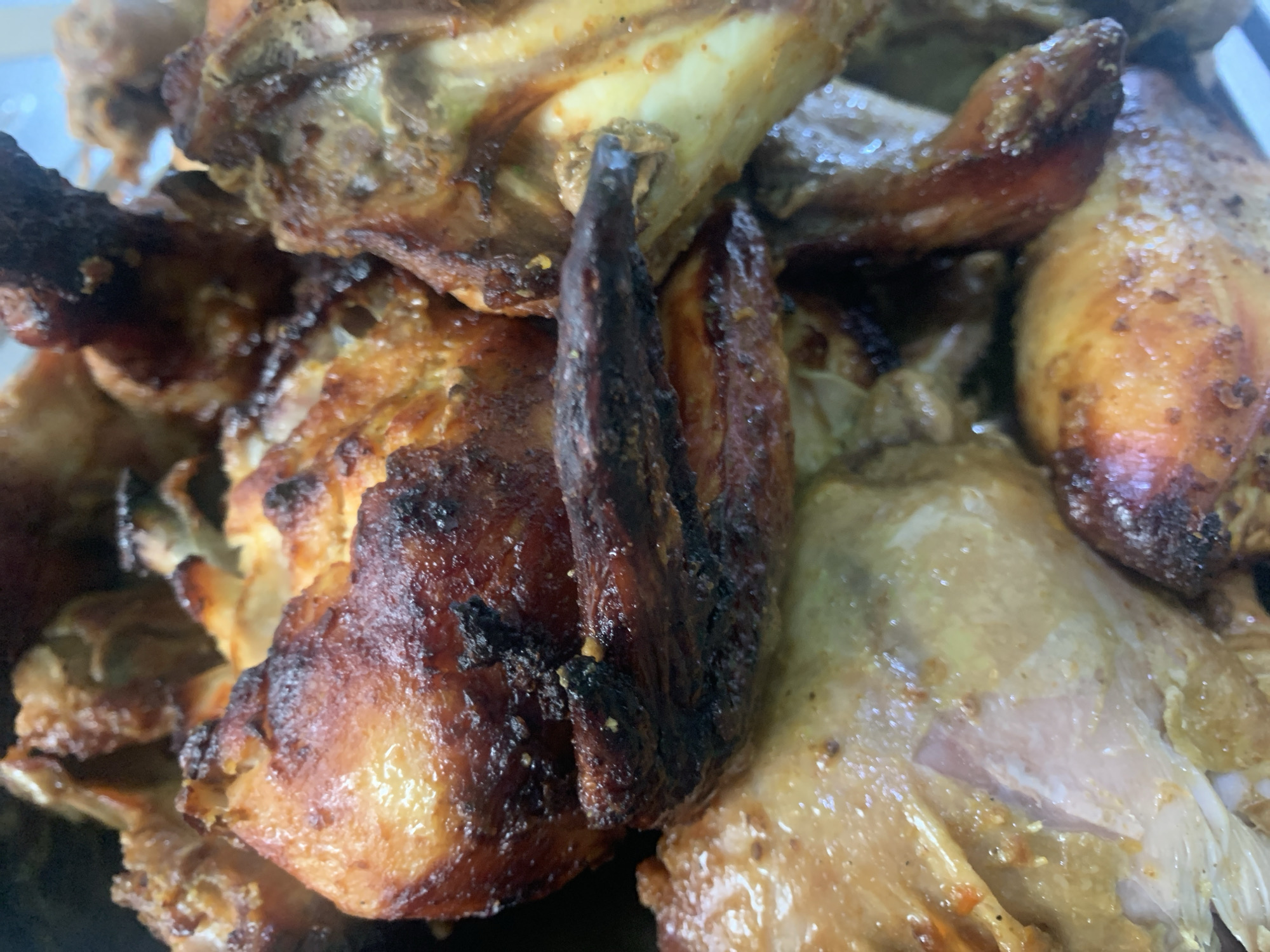 A close-up shot showcases a pile of roasted chicken pieces. The chicken exhibits a golden-brown, slightly charred skin, with visible seasoning and glistening rendered fat. The meat appears tender and juicy, with some portions revealing the white flesh underneath. The arrangement is haphazard, suggesting a serving dish or a container filled with the cooked chicken. The background is dark and indistinct, focusing all attention on the food. The image is likely taken indoors, possibly in a kitchen or dining area.