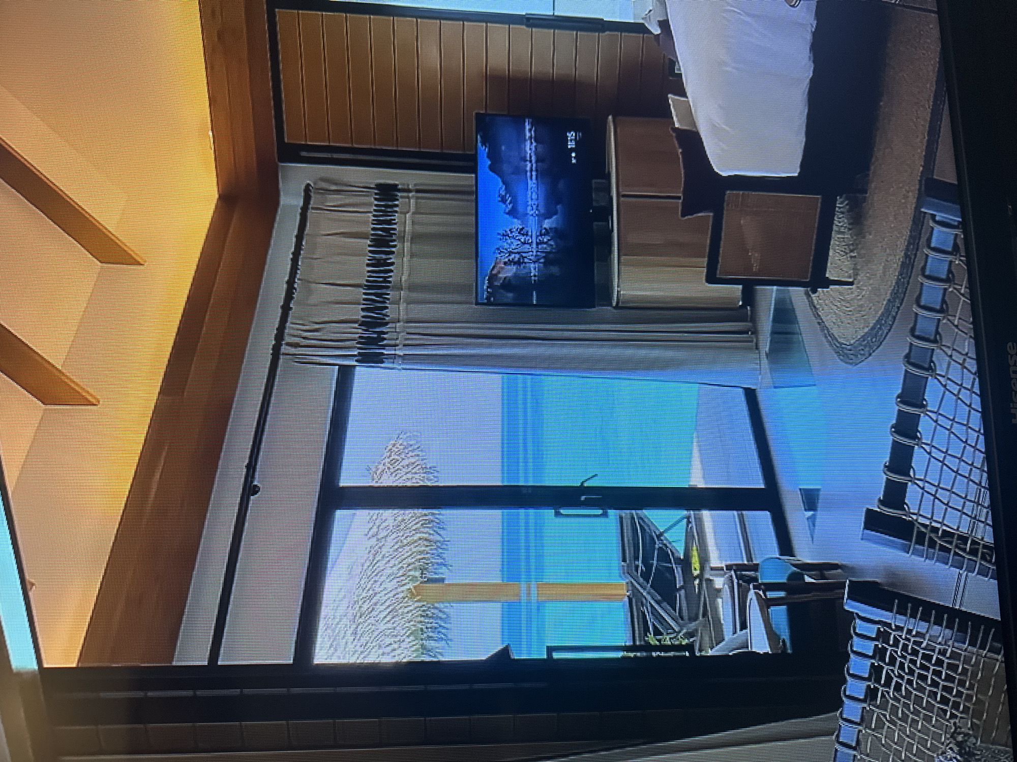 This is a photograph of a luxurious hotel room with a view of the ocean. The room is decorated in a modern style with wooden accents. There is a large sliding glass door that opens onto a balcony overlooking the turquoise water. A TV is mounted on the wall, and a bed is visible in the corner of the room. The scene suggests a tropical or seaside resort setting. There is no indication that this location is in Kyiv, Ukraine; it appears to be a beach resort.