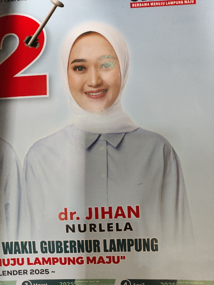 The image displays a close-up photograph of a promotional poster or calendar, likely from Selagai Lingga, Indonesia. The central figure is a smiling woman, identified by the visible text as dr. Jihan Nurlela, who is wearing a white hijab and a light-colored, possibly pale blue, collared shirt. Her expression is friendly and approachable.
To the left of the woman, a large, partially visible red number "2" is depicted, with a nail appearing to be hammered into it. The background is a light, muted blue or gray.
Prominent text below the woman's portrait reads "dr. JIHAN NURLELA" in red, followed by "WAKIL GUBERNUR LAMPUNG" (Deputy Governor of Lampung) and "MENUJU LAMPUNG MAJU" (Towards Prosperous Lampung) in a similar style. At the top right, the phrase "BERSAMA MENUJU LAMPUNG MAJU" (Together Towards Prosperous Lampung) is also visible. The bottom section of the poster shows calendar details, including "KALENDER 2025 ~" and specific months "Maret 2025" (March 2025) and "April 2025". Some minor blemishes or wear marks are present on the poster, particularly on the woman's face and shirt, suggesting the condition of the printed material. The image appears to be a political or public service announcement poster for the Lampung region.