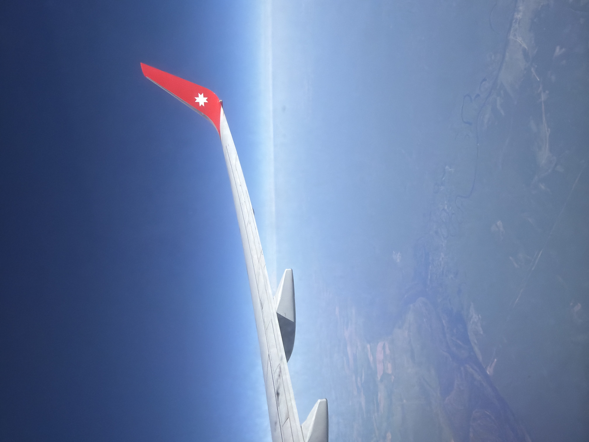 An airplane wing with a red tip and a white eight-pointed star on it is visible against a blue sky and landscape. The landscape appears to be forested with some rivers or waterways visible. The location is implied to be near Domodedovo, Russia, based on the airline's flag on the tail.