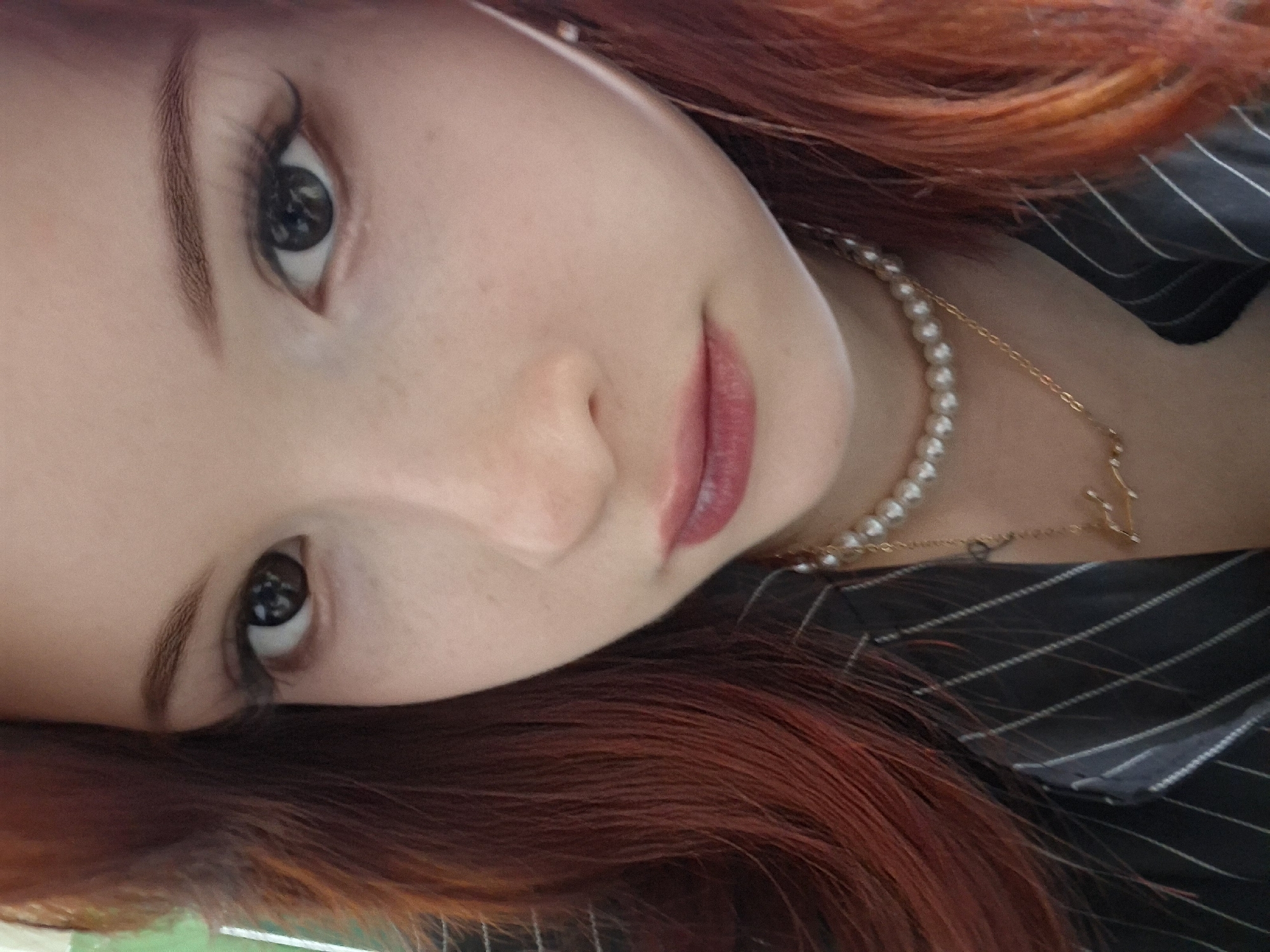 A close-up, slightly tilted portrait of a woman with red hair. She is wearing a pearl necklace and a striped black and white shirt. The focus is on her face, highlighting her eyes and lips. No specific details indicate the location is Chaikovsky, Russia.