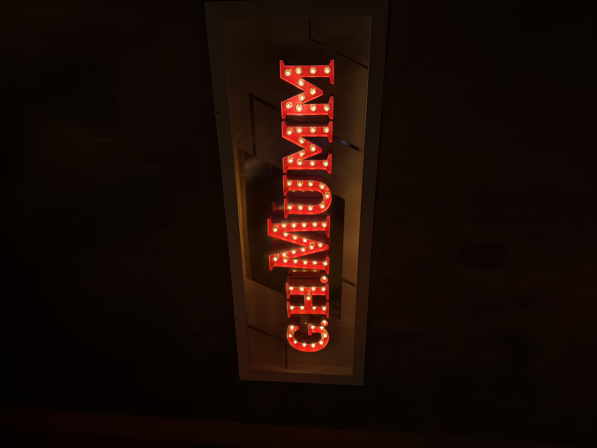 The image shows a vertical red neon sign with illuminated bulbs, spelling "CHUMURI" in block letters. The sign is mounted within a light-colored rectangular frame against a dark background, possibly a wall. The photo seems to be taken in a dimly lit indoor environment. It is located in Sofia, Bulgaria.
