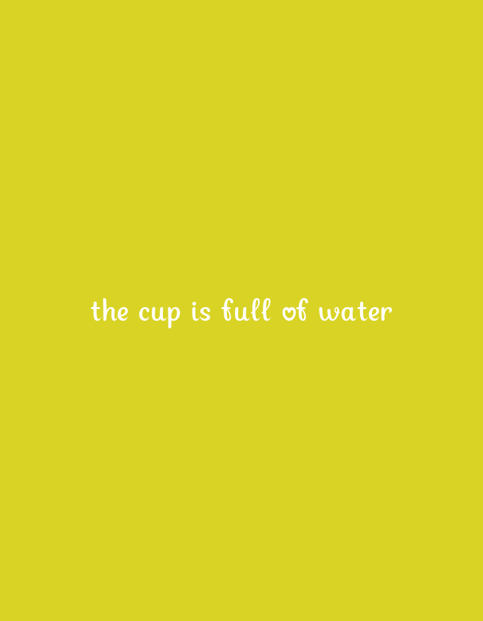 The image is a close-up, medium shot of text on a yellow background. The text, written in white, cursive font, reads "the cup is full of water". There is a small heart symbol between "full of" and "water". The background is a solid, bright yellow color. No location in the city of Unknown, Unknown can be determined from the image.
