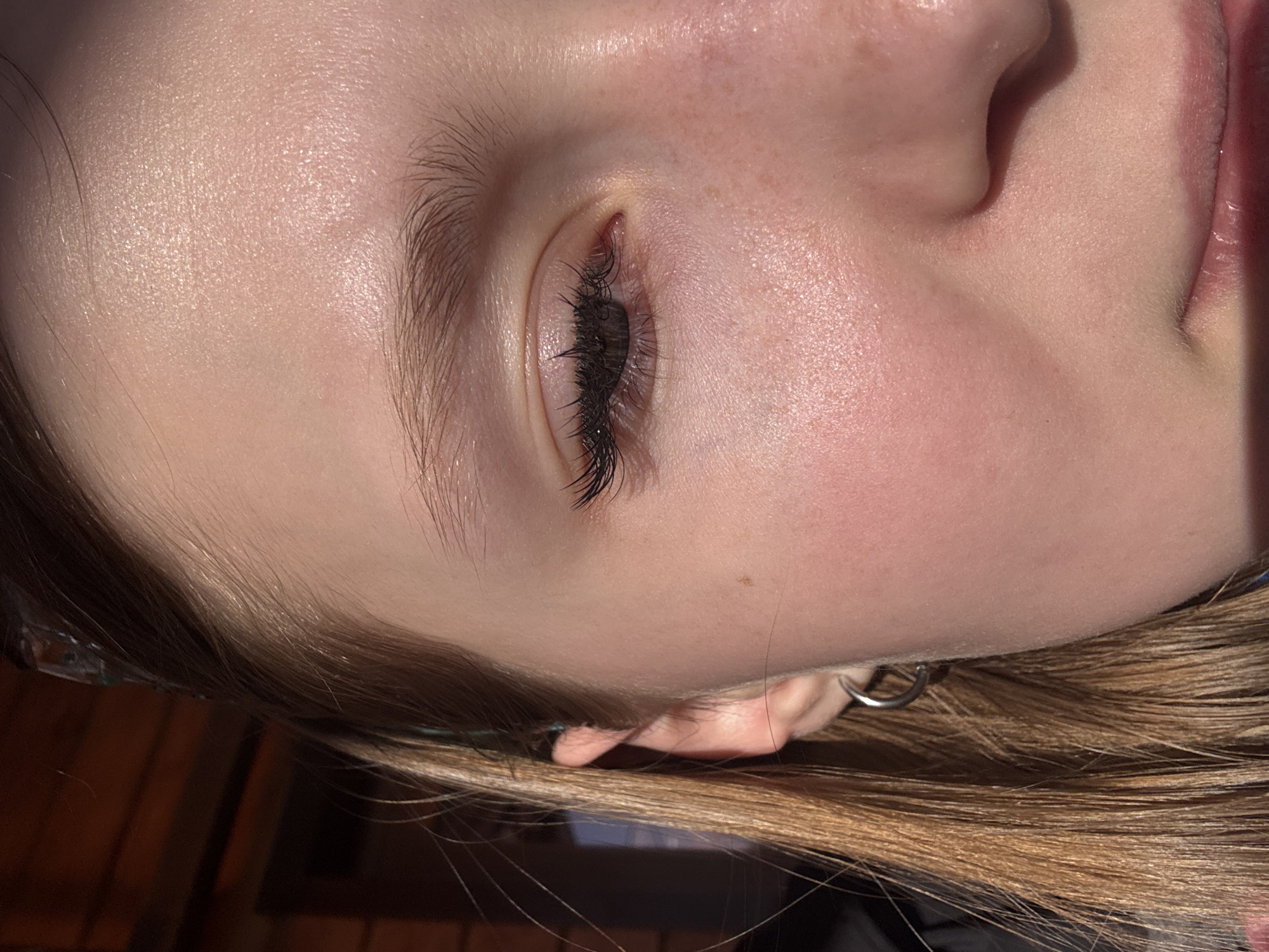 A close-up image shows a person's face, likely female, with light skin, blonde hair, and a closed eye with dark eyelashes. The face is slightly turned towards the right. The lighting is bright and reflects on the skin. The environment appears to be indoors, based on the background. No information indicates that the image was taken in Gory, Russia.