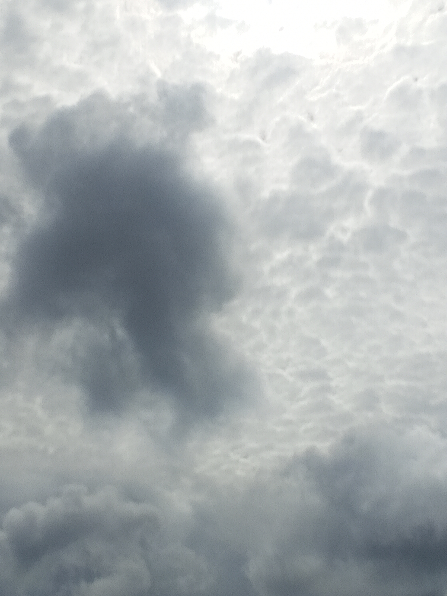 The image depicts a cloudy sky over Altagracia, Venezuela. The clouds are a mix of dark gray and white, with the sun attempting to break through the overcast. The overall impression is that of a potentially stormy or overcast day. There are no discernible people, subjects, objects, actions, or interactions visible in the image. The focus is solely on the atmospheric conditions.