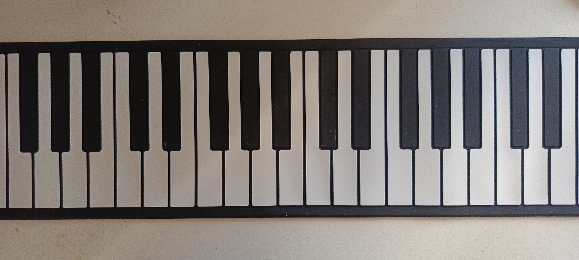 An overhead shot shows a portion of a black and white keyboard for a piano. The keyboard is flat and appears to be on a light-colored surface. The keyboard is composed of a series of black keys interspersed with white keys. The black keys are narrower and shorter than the white keys, and they are positioned in groups of two and three. The white keys are rectangular and extend further down than the black keys. The keyboard is framed by a black border. The image does not contain any people or actions. The location of this image in Baku, Azerbaijan cannot be determined from the visual information provided.