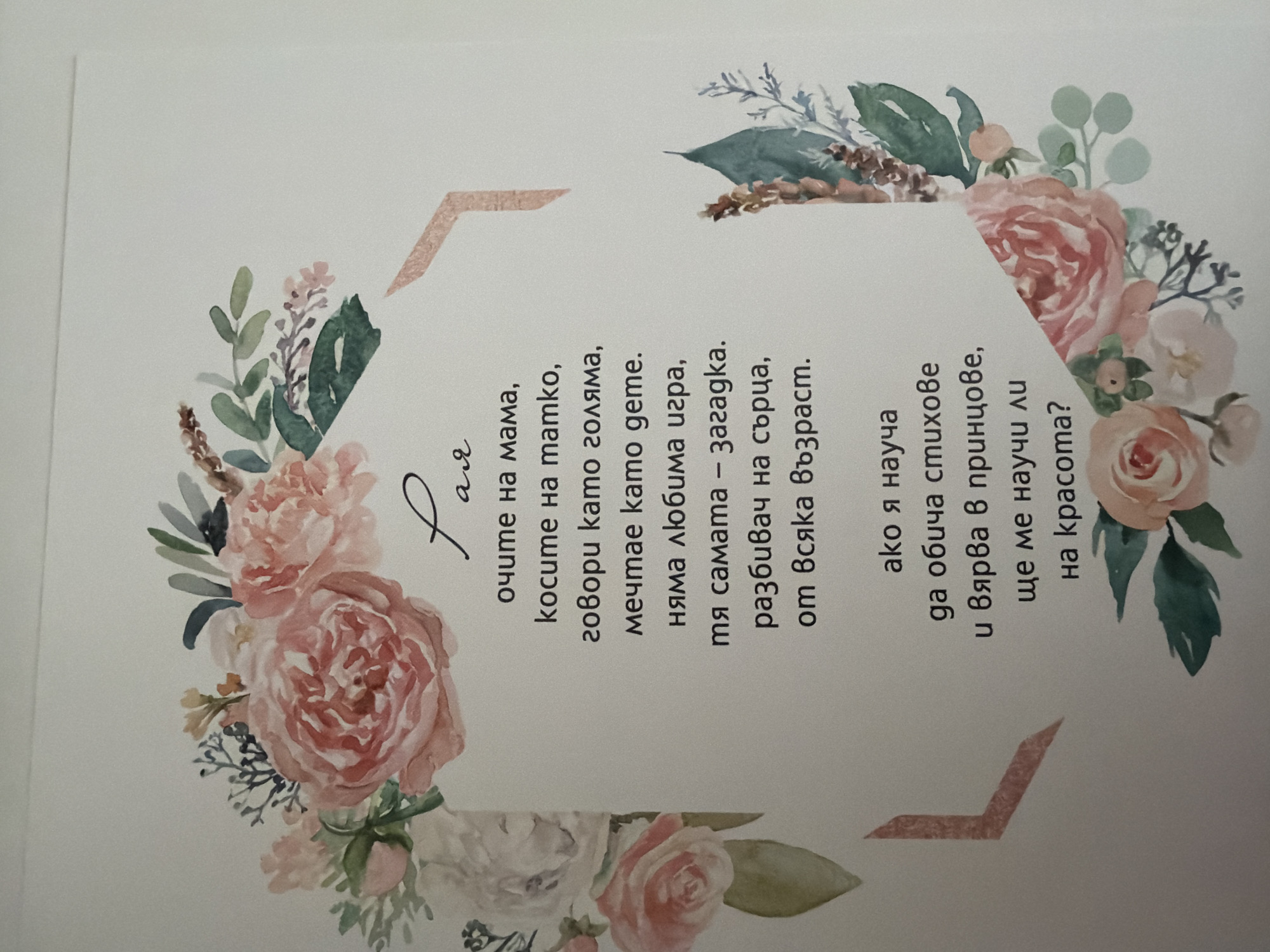 The image displays a poem written in Bulgarian, framed by a watercolor floral border. The poem is centered on a white background. The floral arrangement features roses and greenery in shades of pink, peach, and green. The poem is written in a dark script, with the first word, "Мамо," (Mama) appearing larger and more stylized than the rest of the text. The text is arranged in several lines, forming a relatively compact block. The poem appears to be a tribute to a mother.
There is no discernible location in the city of Pazardzhik, Bulgaria, or any other city or town depicted in the image. The image is a close-up of a printed or written piece of material, possibly a card or a page from a book.